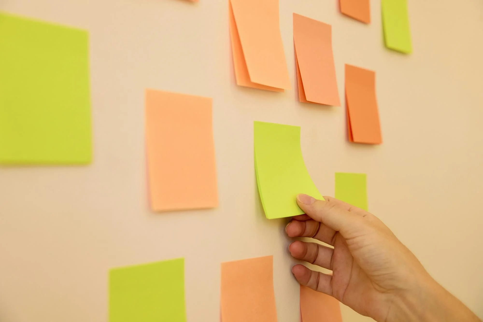 A person placing a yellow sticky note on a wall covered with various orange and yellow sticky notes arranged for a planning or brainstorming session.