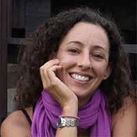 Smiling woman with curly hair wearing a purple scarf and a watch, resting her chin on her hand.