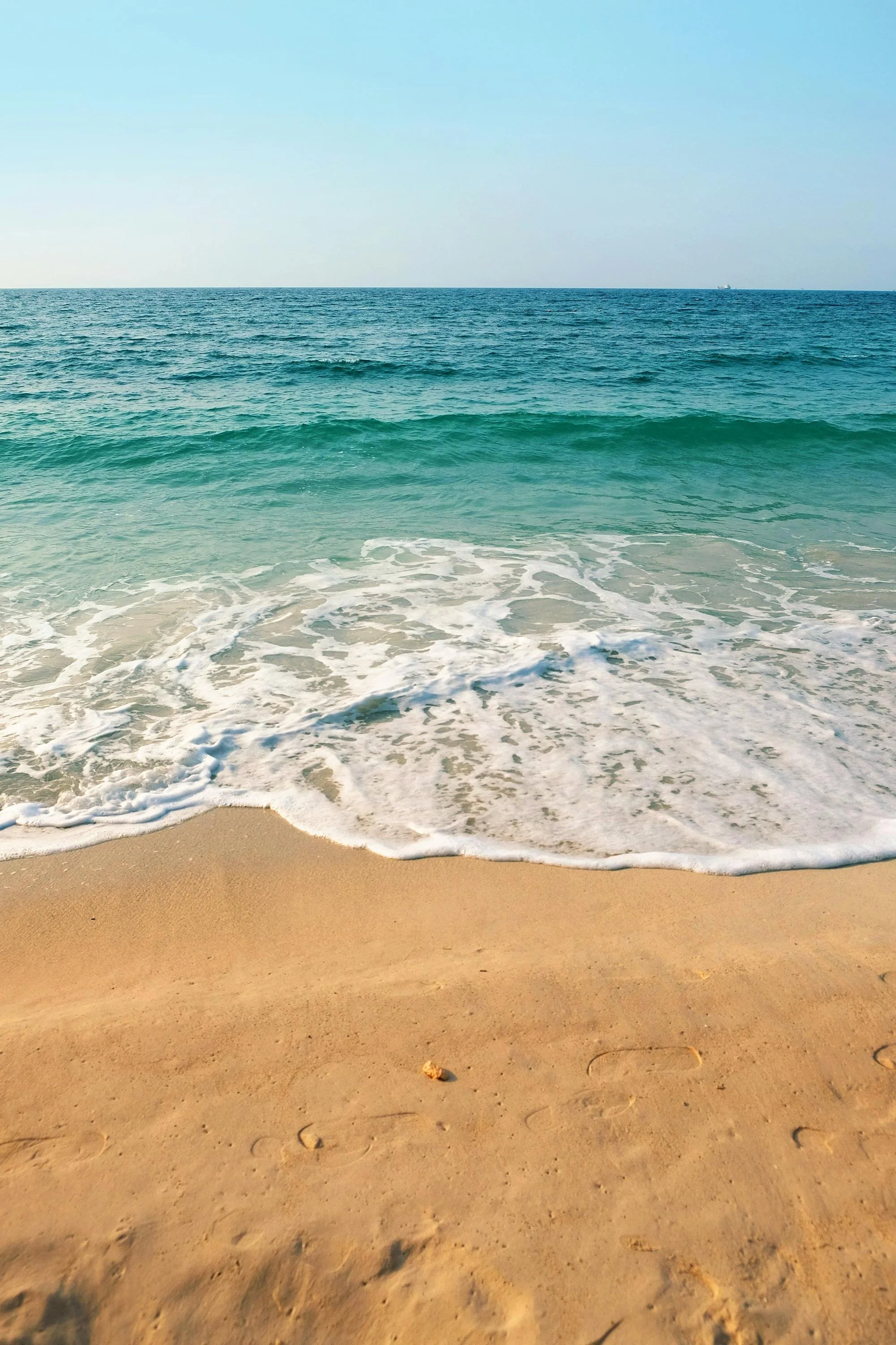 Sandy beach with gentle ocean waves and a clear blue sky