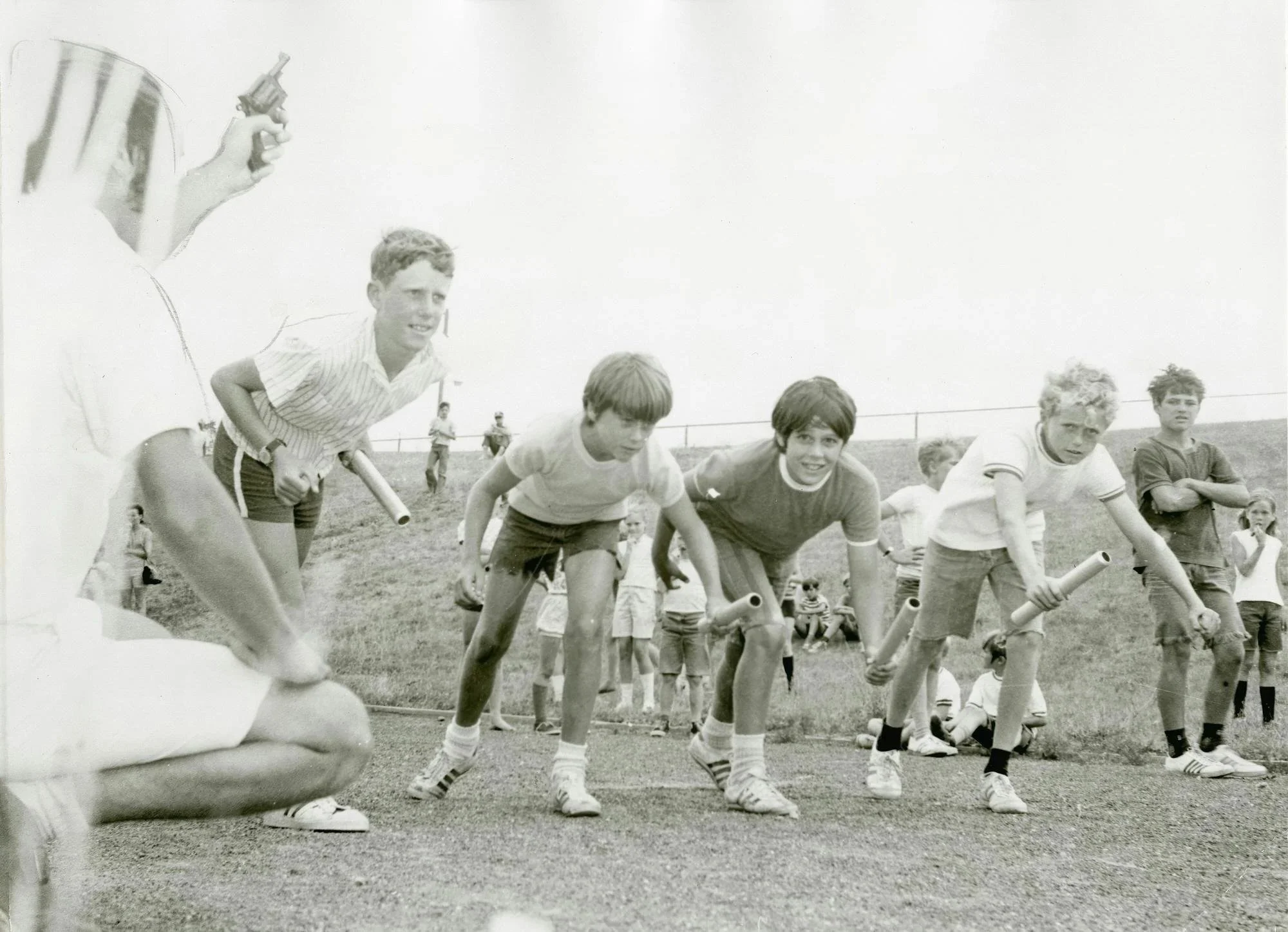 Young boys dressed in athletic clothing participating in a rodeo event, preparing to run through a chute with tubes on a grassy field.