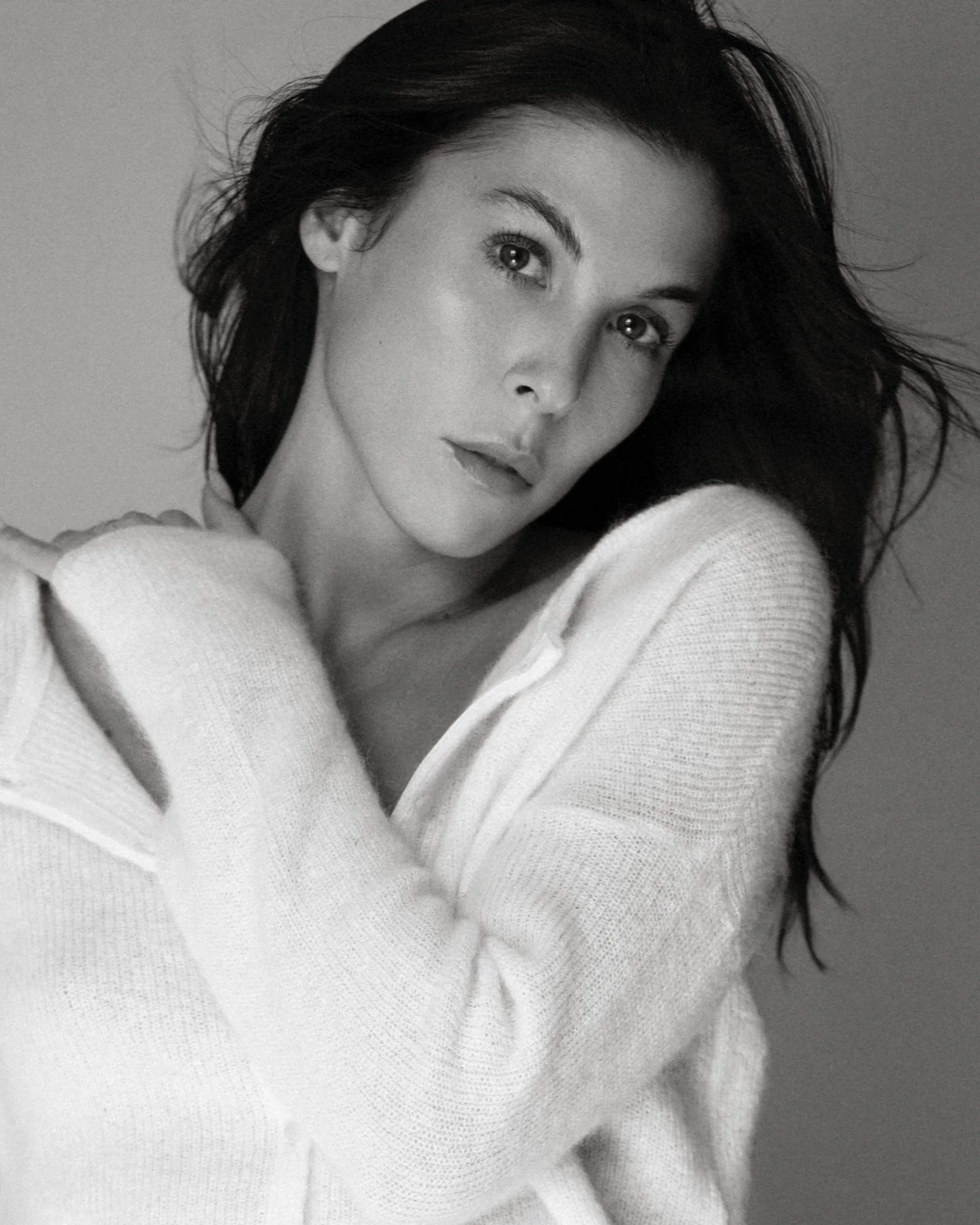Black and white close-up portrait of a woman with long dark hair, wearing a light-colored sweater, looking directly at the camera with a calm expression.