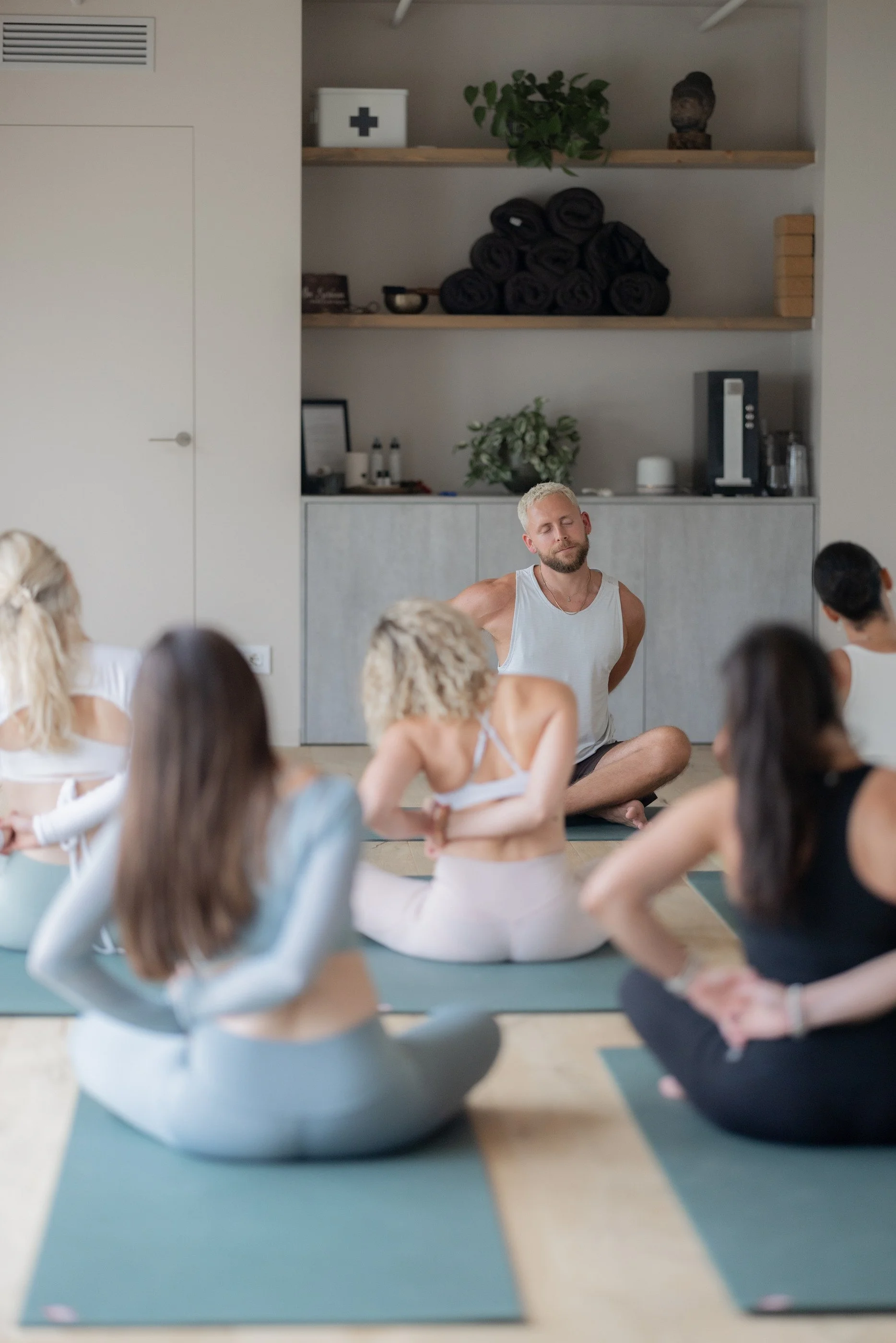 Tom guiding a seated shoulder mobility exercise with a group of students in a studio.