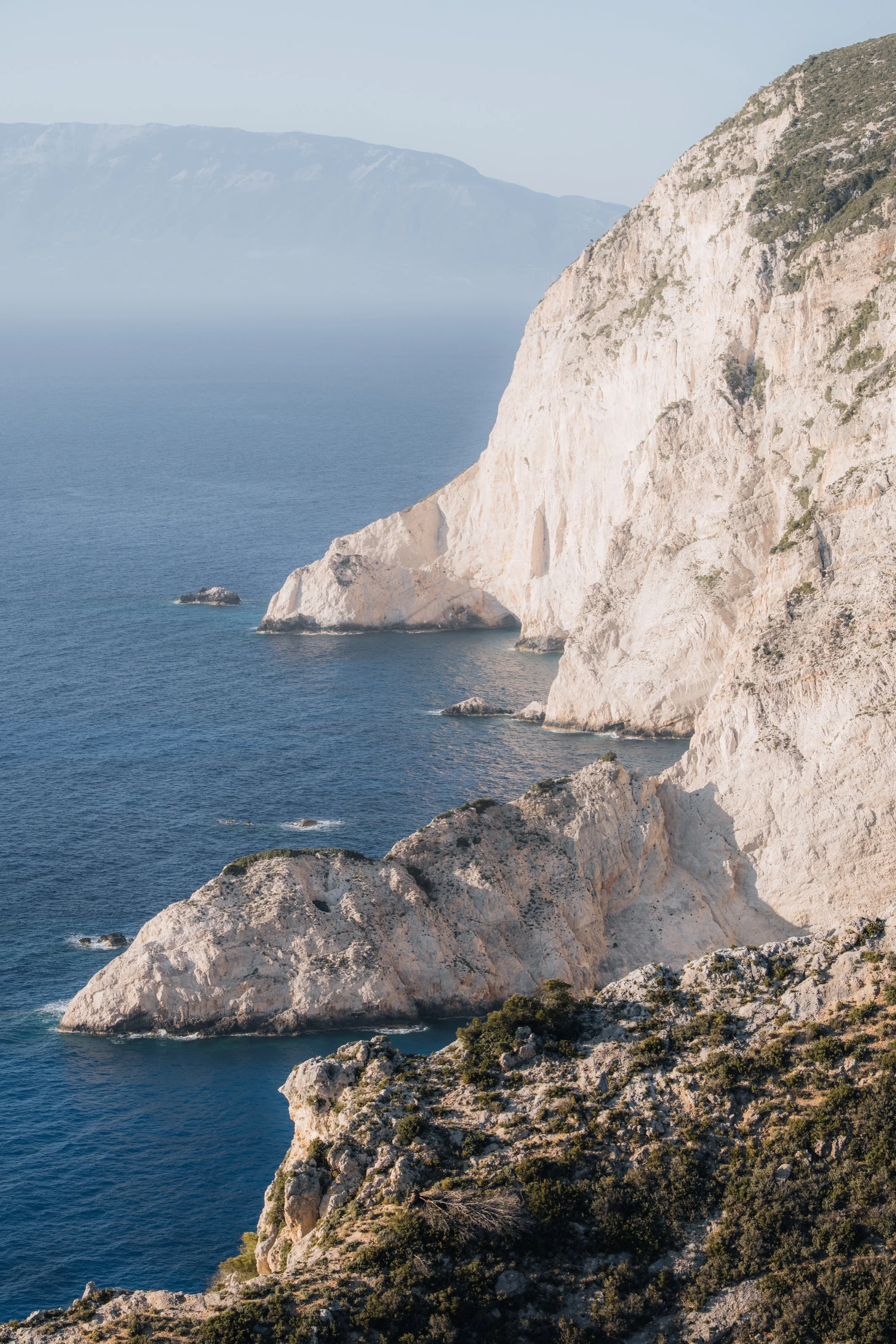 Sunlit limestone cliffs rising above deep blue sea on the Greek coast.