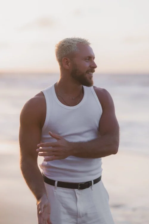 Tom Wilson-Leonard smiling beside the sea in soft evening light.