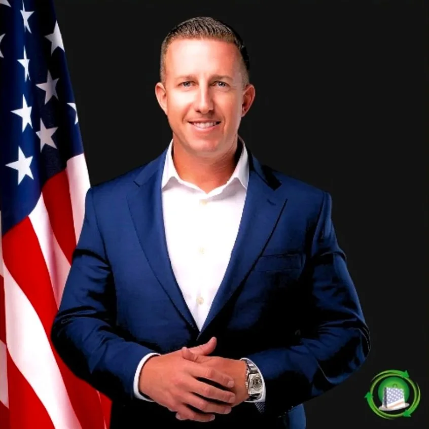 A man in a blue suit and white shirt standing in front of an American flag against a black background.