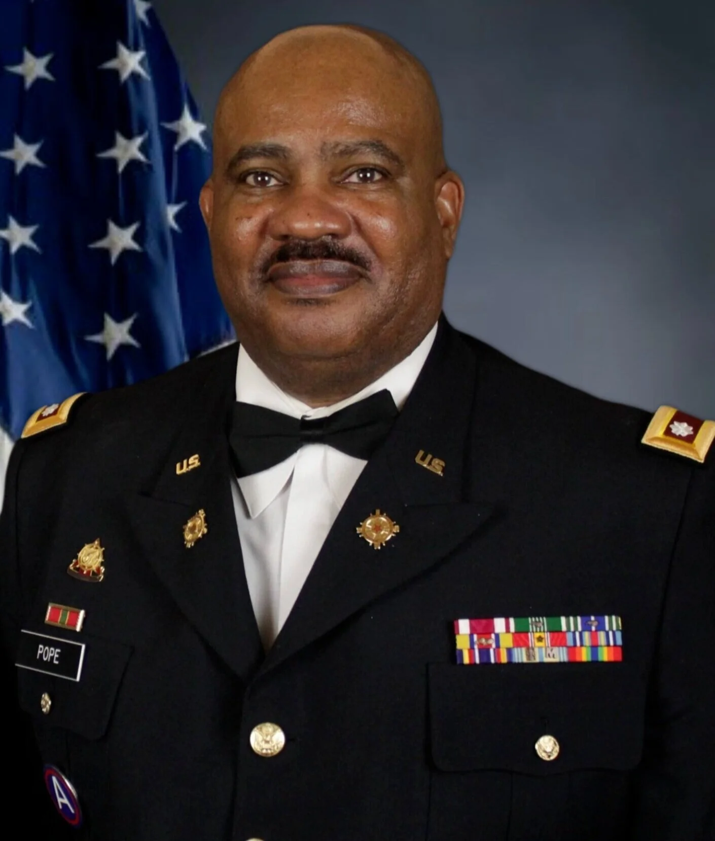 A man in a U.S. military uniform in front of an American flag.