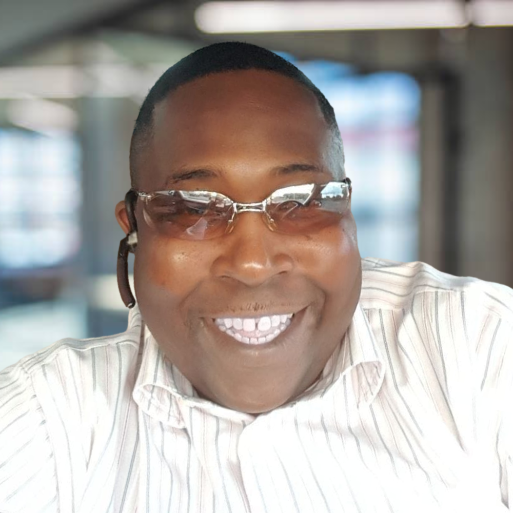 A smiling man wearing sunglasses and a striped white shirt.