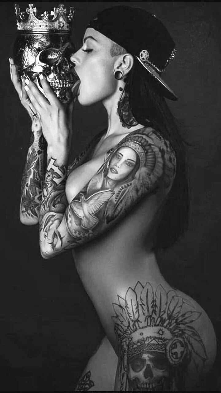 Person with tattoos holding a skull wearing a crown, in black and white.
