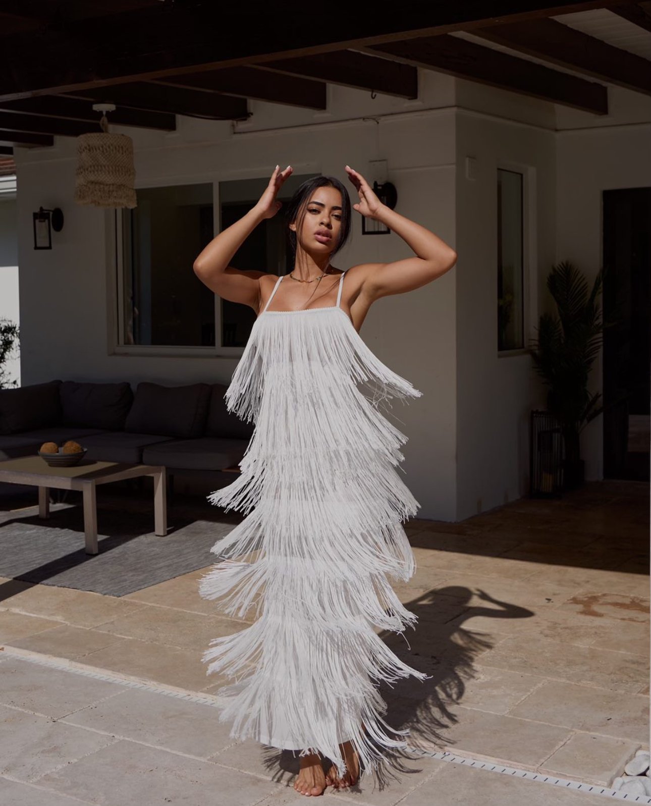 A woman with an afro hairstyle wearing a brown t-shirt and high boots, sitting on a block against a red background.