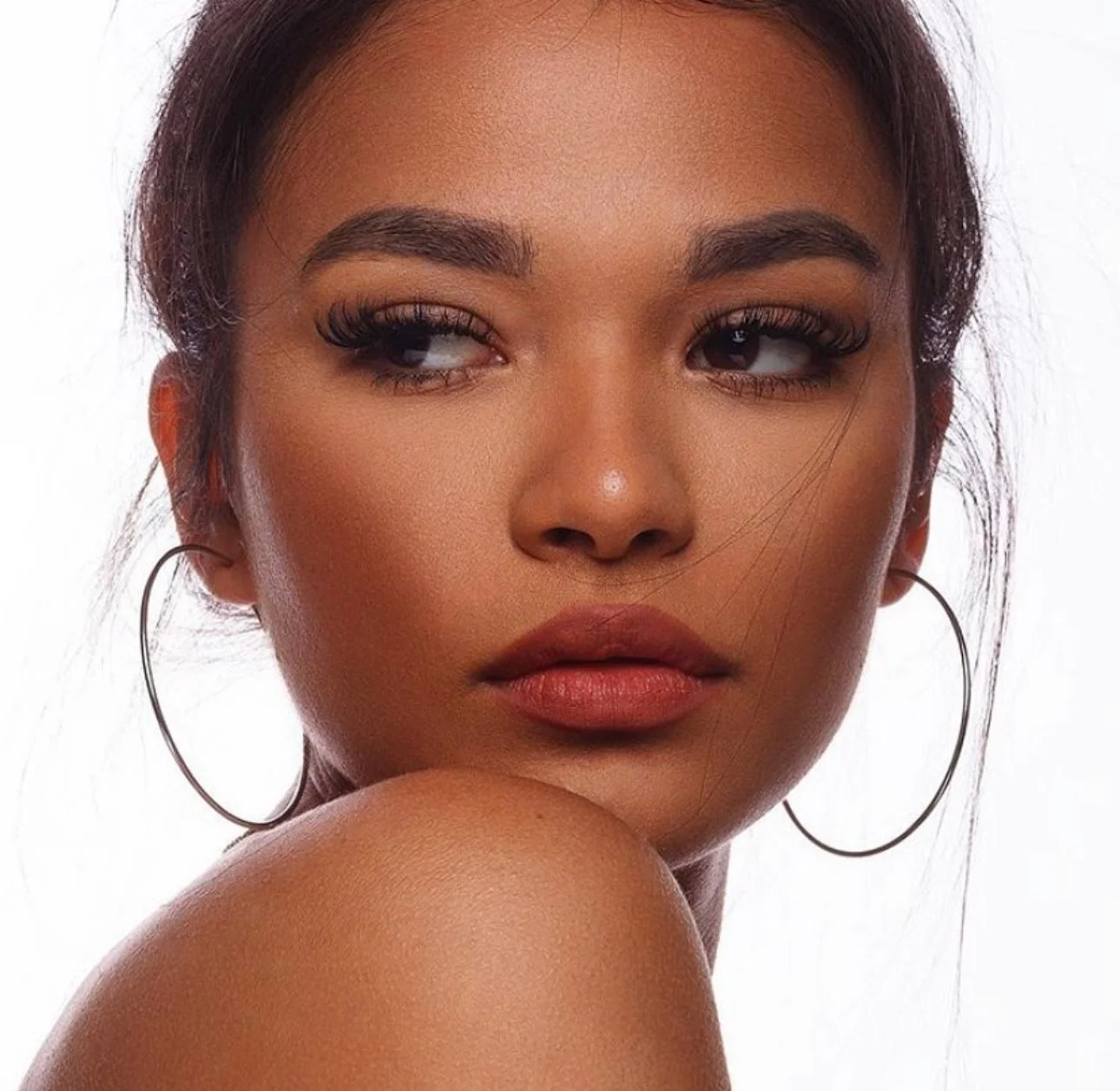 Portrait of a woman with hoop earrings and lipstick looking sideways.