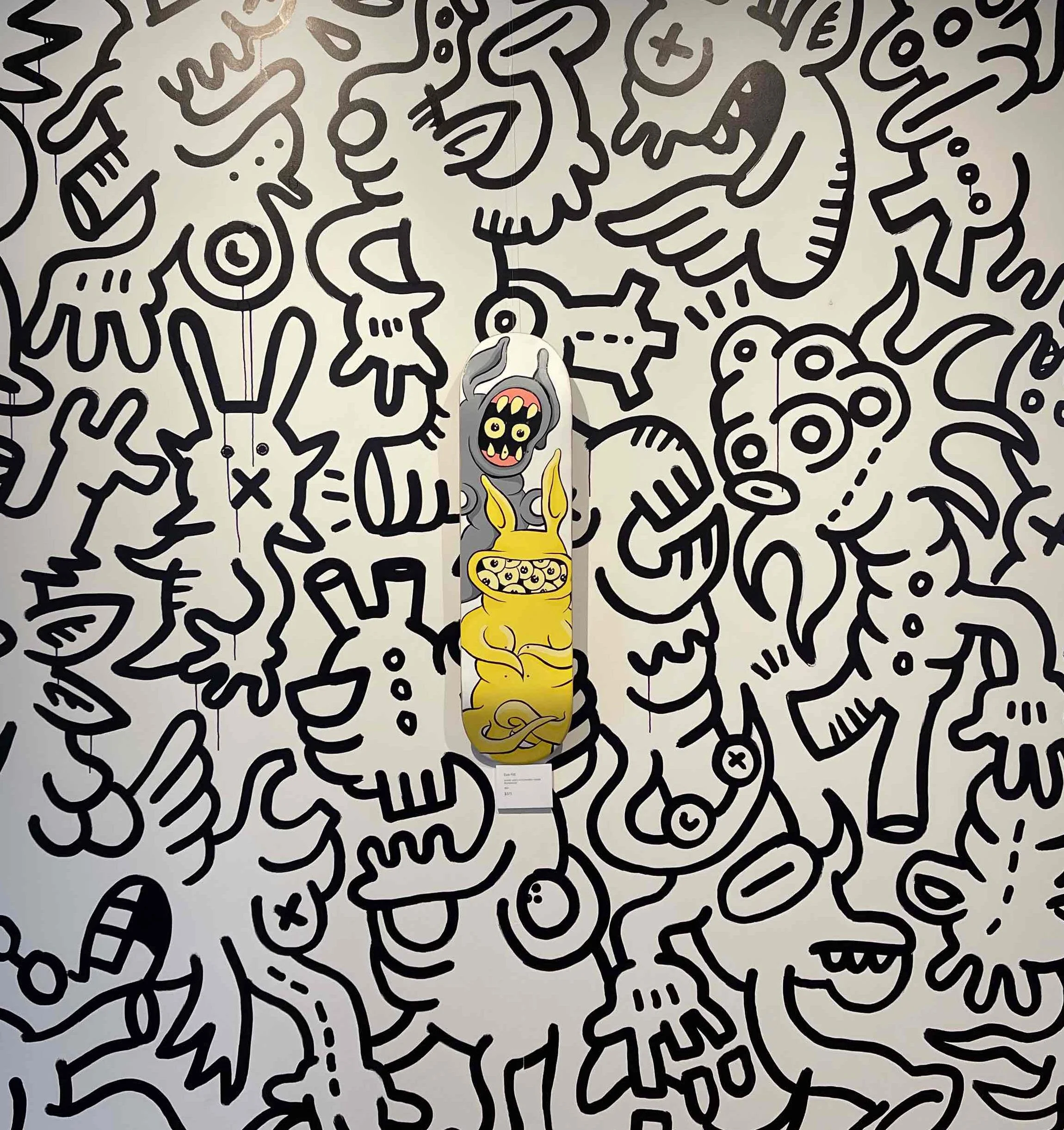 Skateboard hung on a gallery wall which is painted with a black and white cartoon style graphic