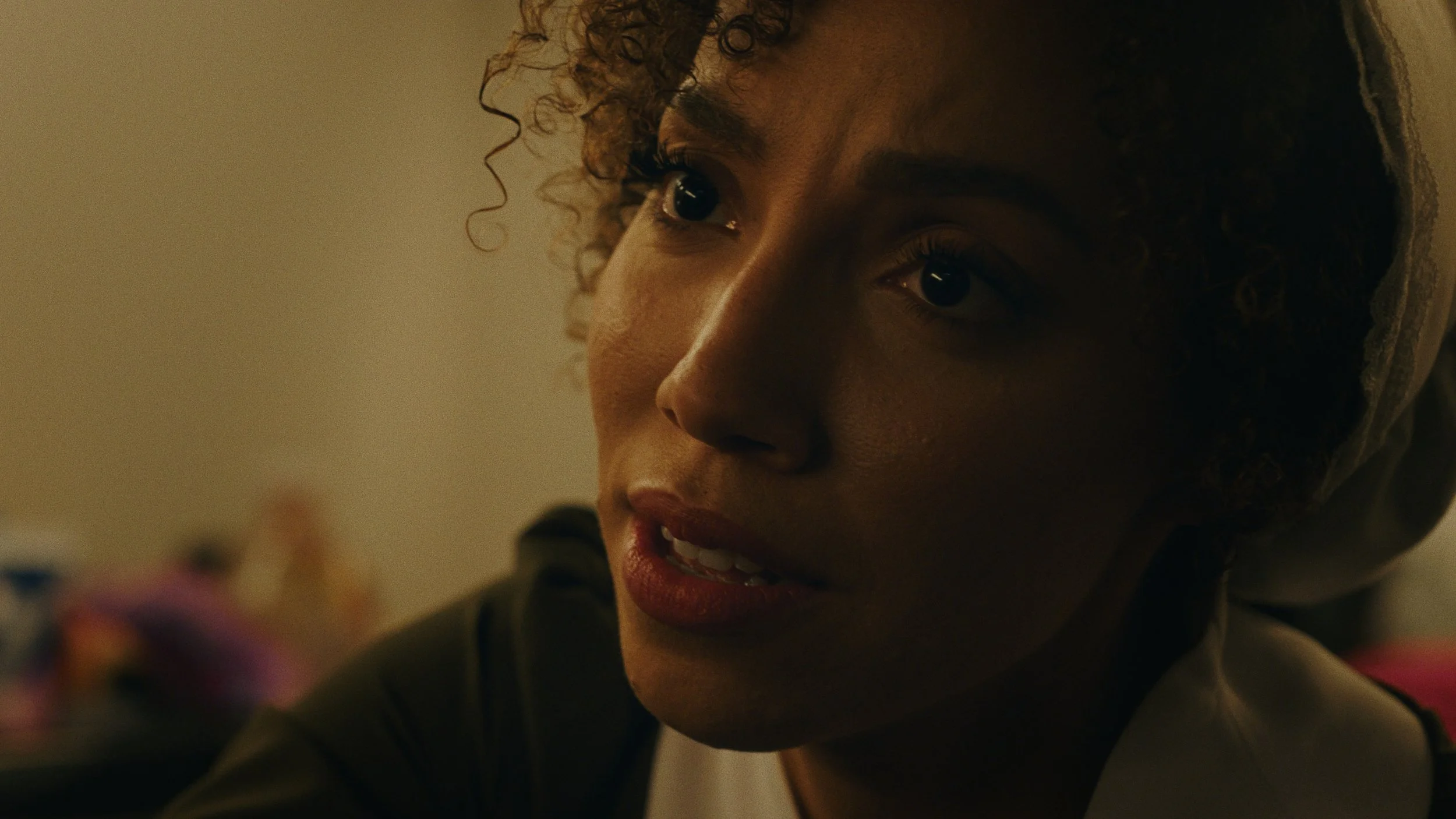 A close-up of a woman with curly hair and dark eyes, smiling slightly and looking at something in her hand.