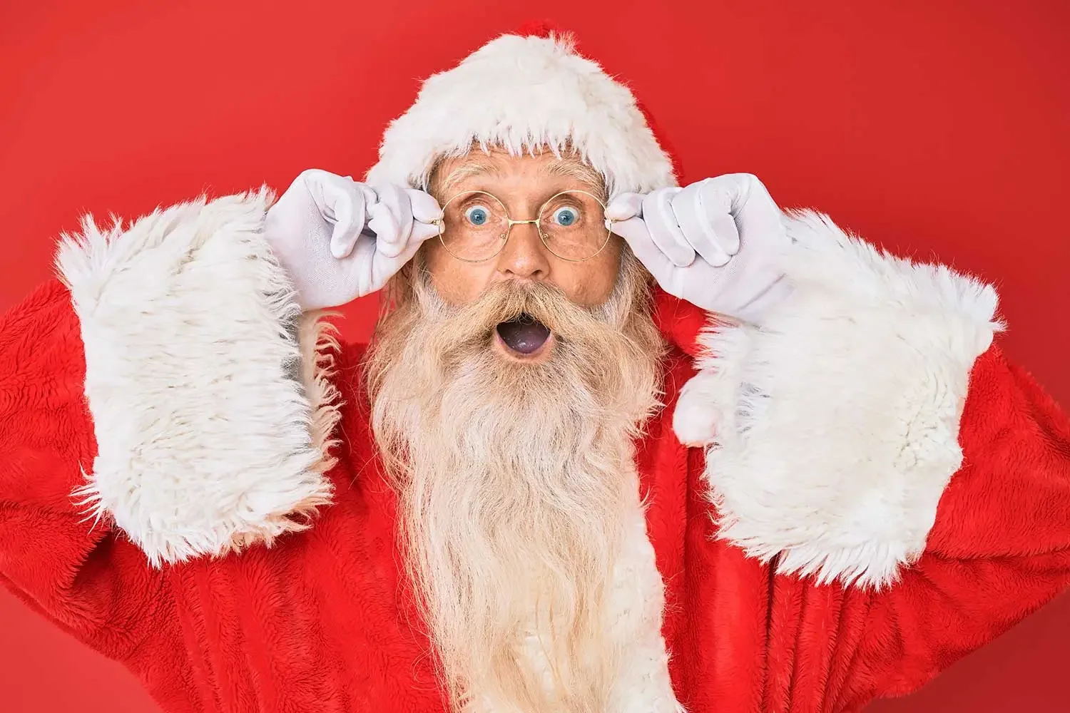 Santa Claus with wide eyes and open mouth holding his glasses