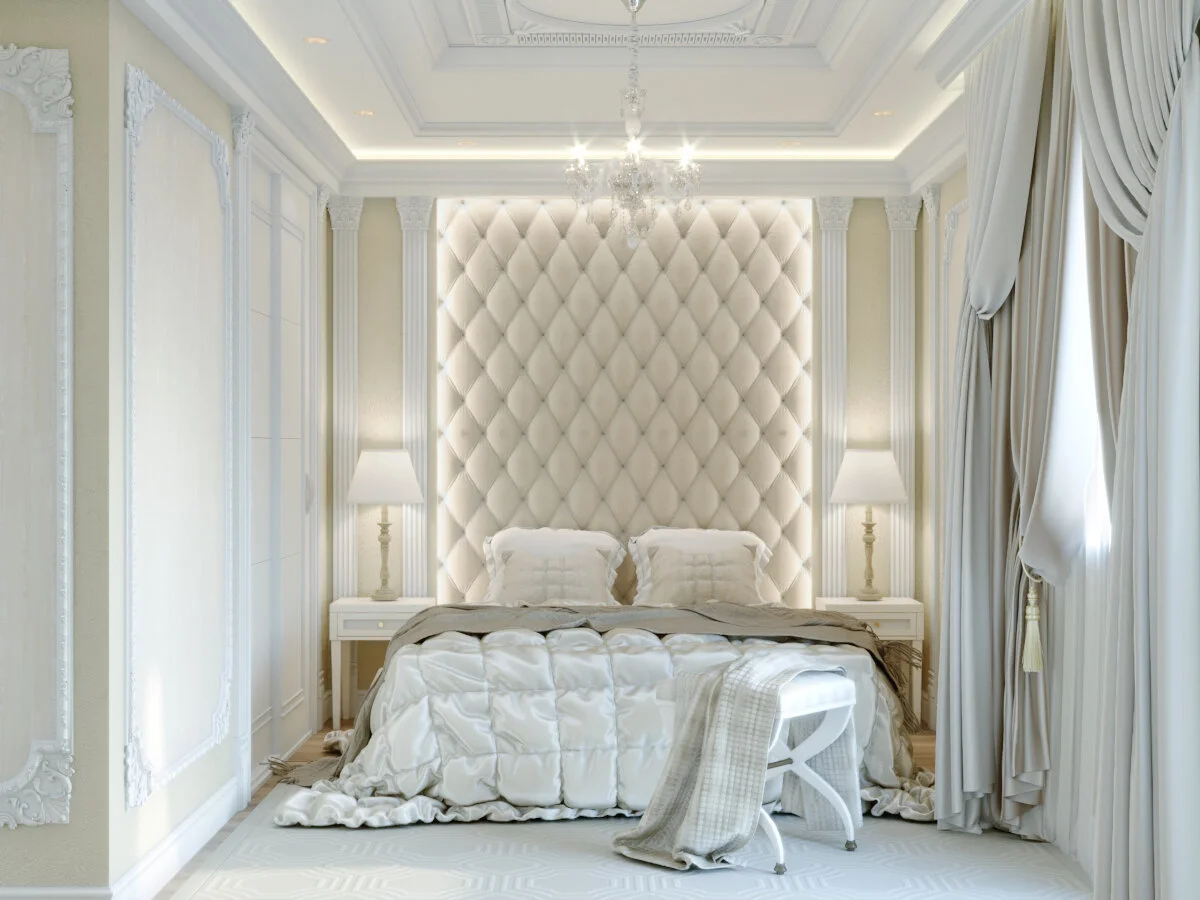 Luxurious bedroom with a large, tufted, cream-colored headboard, two bedside tables with lamps, beige curtains, and a chandelier
