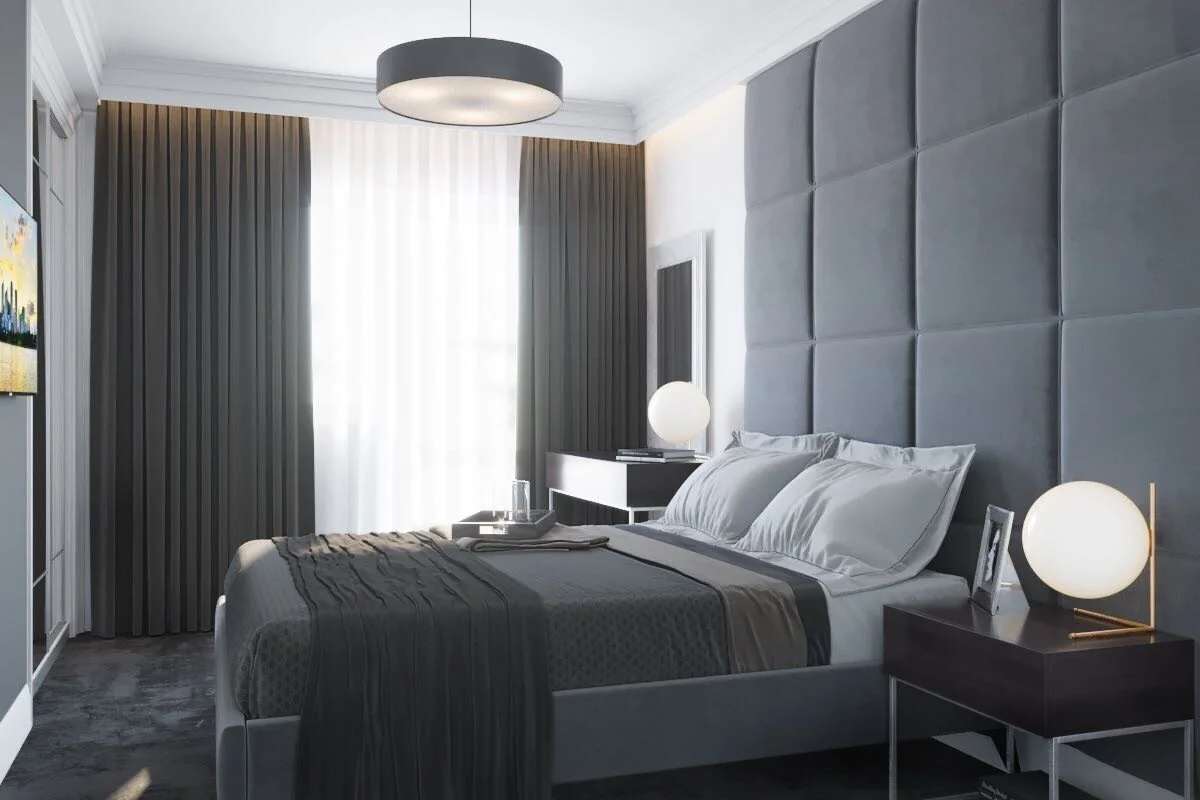 Modern hotel bedroom with gray upholstered headboard, white bedding, dark nightstands with round white table lamps, and a large window with light and dark curtains.