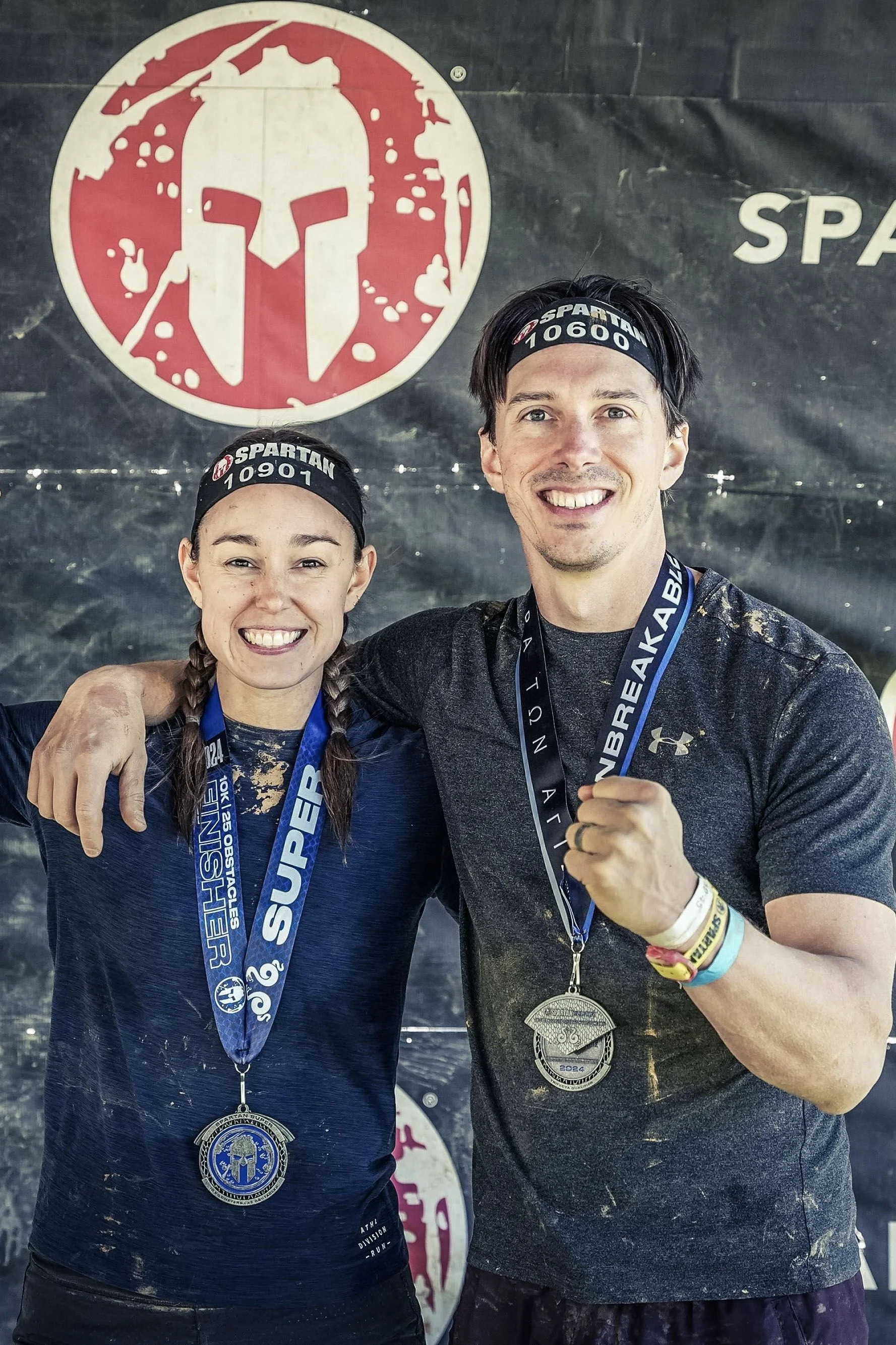 Two people wearing Spartan headbands and medals, posing together after a race with the Spartan logo in the background.