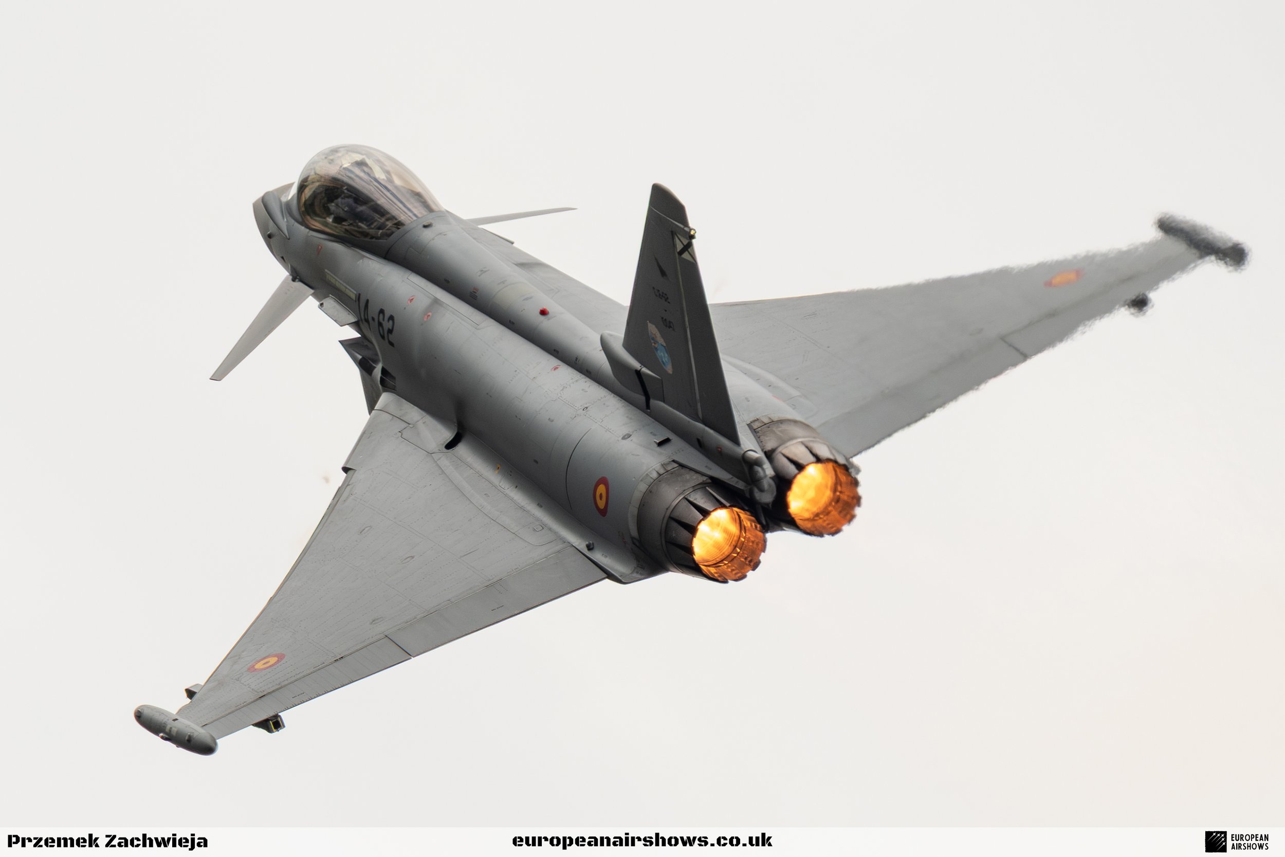 A fighter jet aircraft in flight with afterburners lit, flying against a cloudy sky.