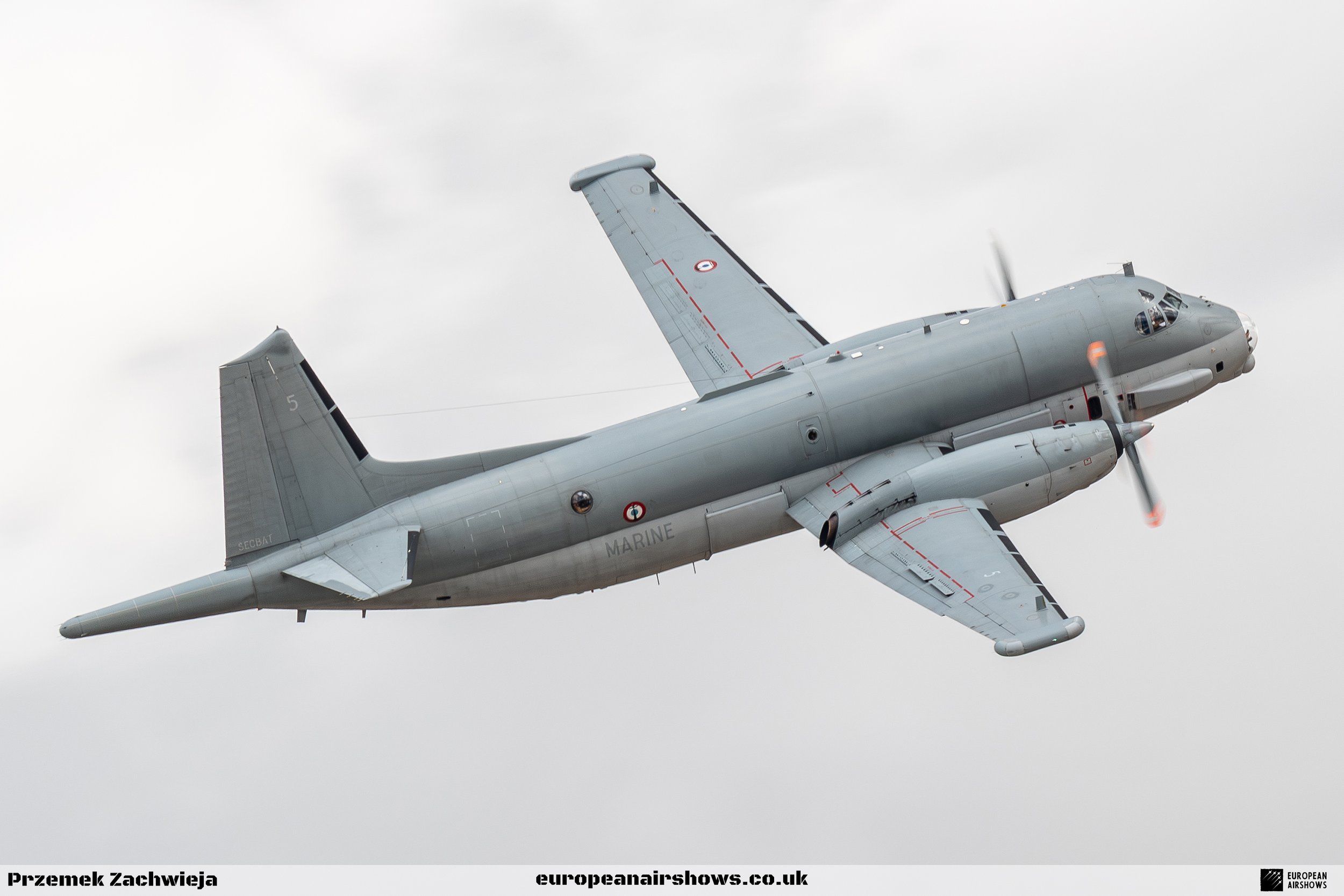 A gray military aircraft flying in cloudy skies.