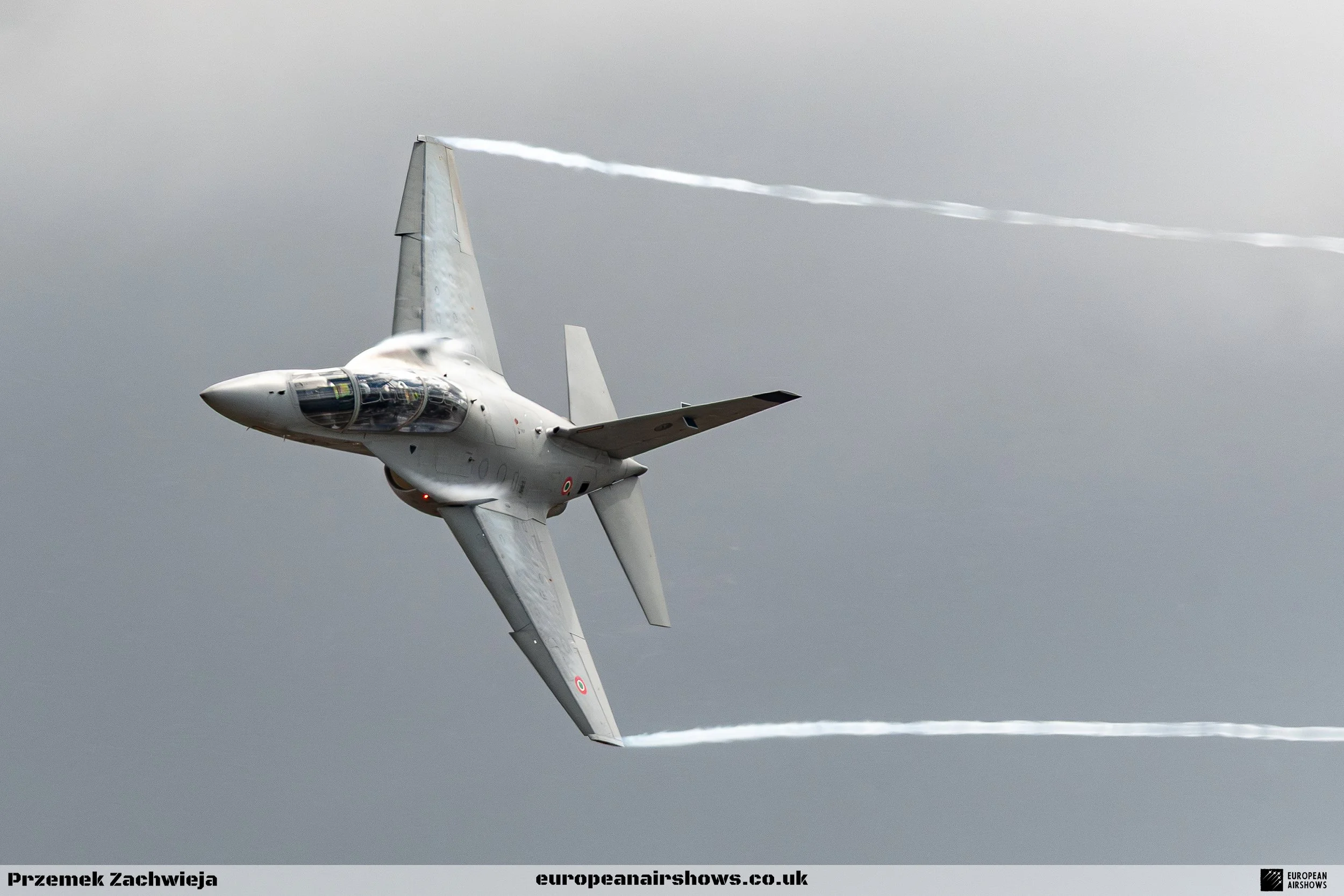 A fighter jet flying at an angle in the sky with contrails behind it.