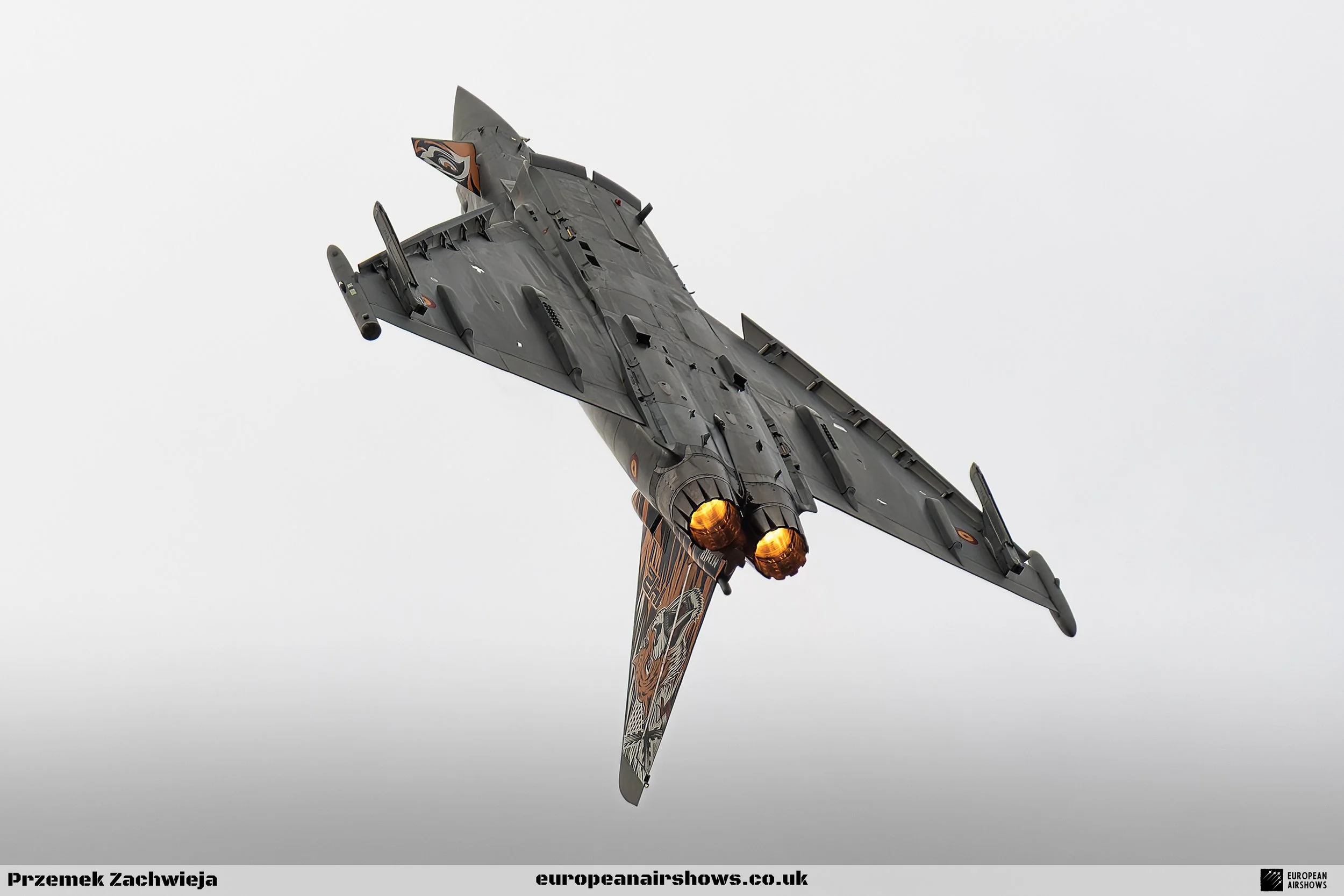 A fighter jet with afterburners ignited, flying against a cloudy sky.