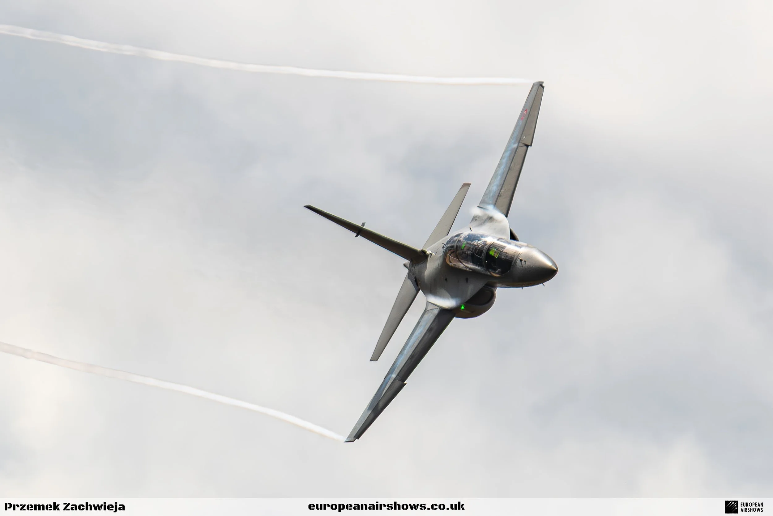 A fighter jet aircraft flying through cloudy sky, leaving vapor trails behind.