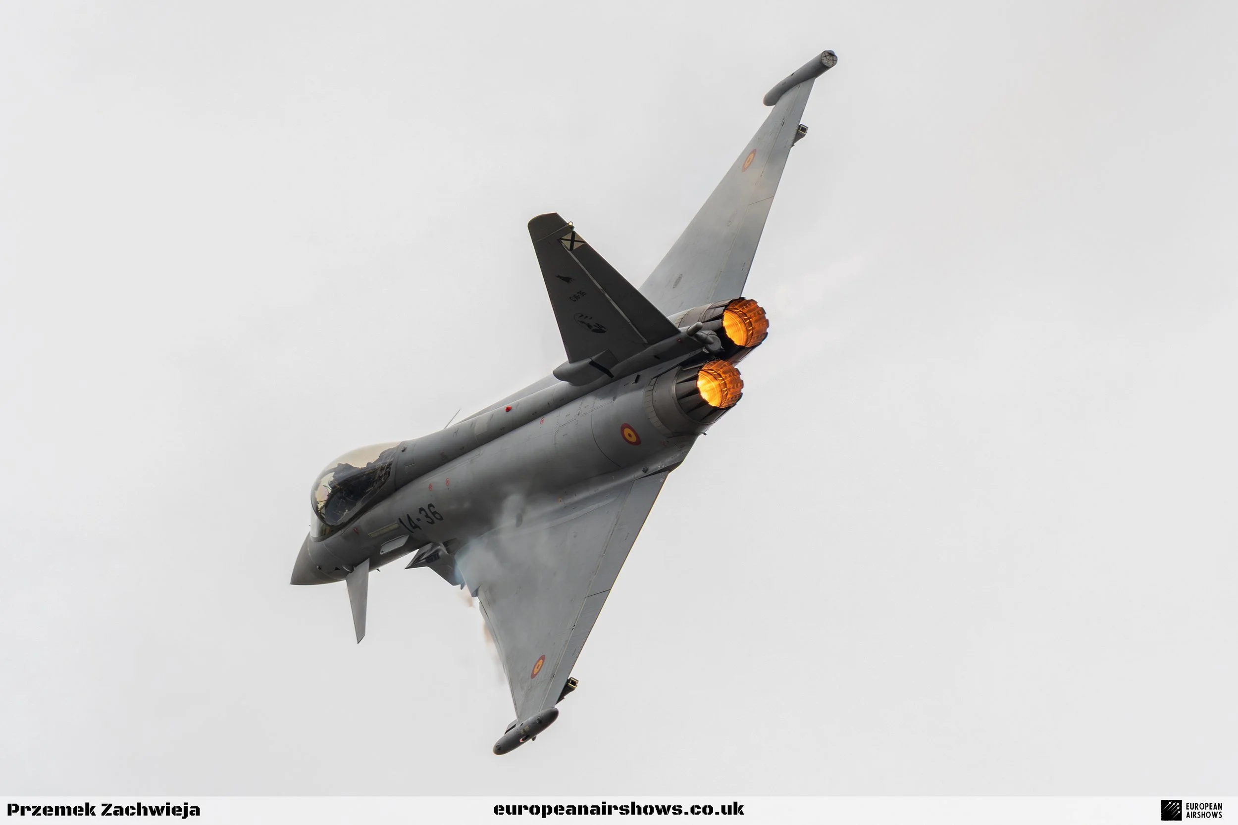 A fighter jet flying at a high altitude with afterburners engaged, emitting bright orange flames, against a cloudy sky.