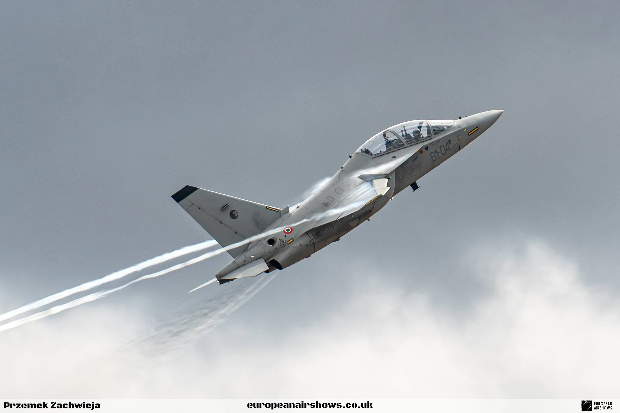 A fighter jet airplane flying in the sky, leaving a contrail behind it, against a cloudy background.