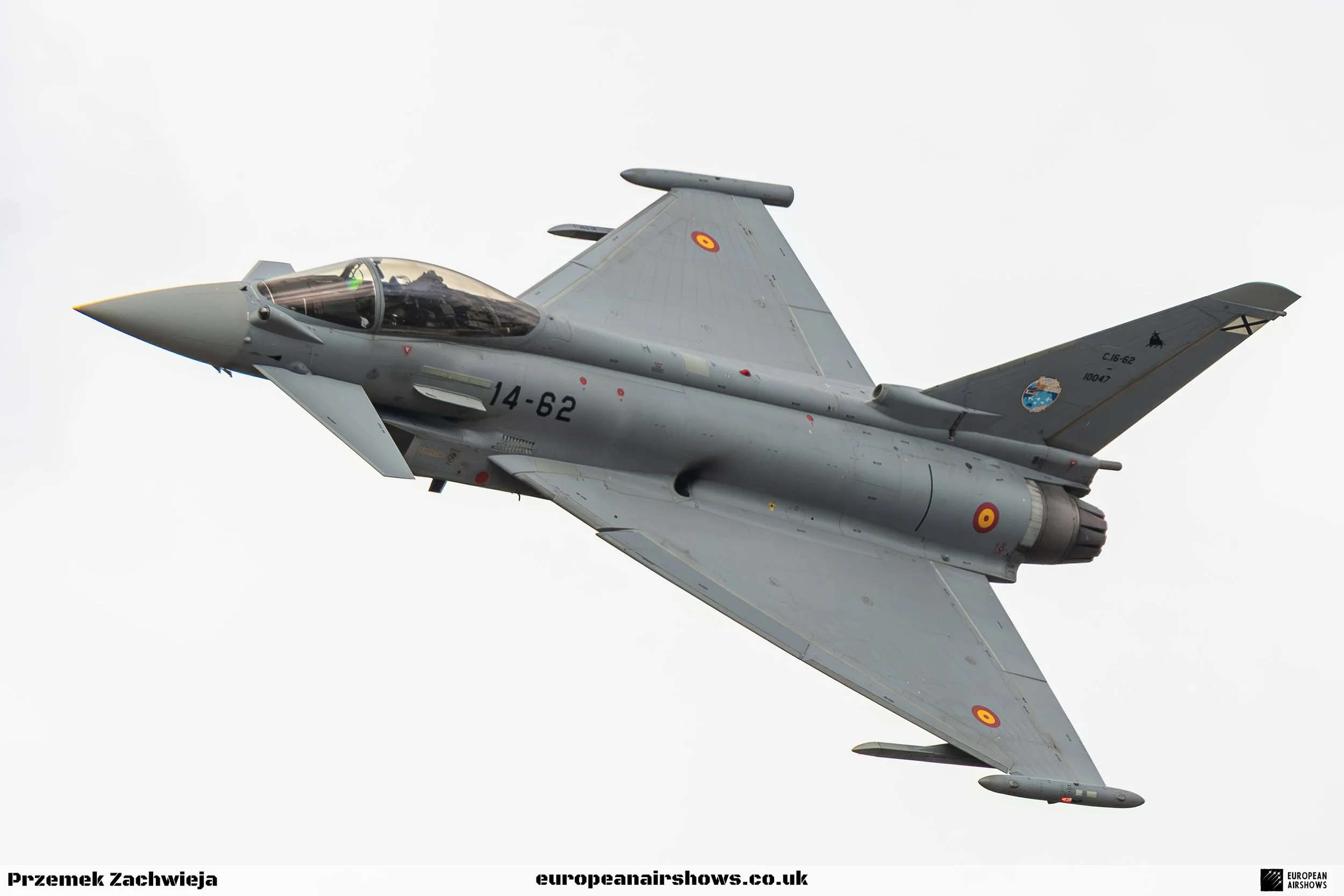 A military jet aircraft flying through the sky, painted in gray, with roundel markings on its wings and fuselage.