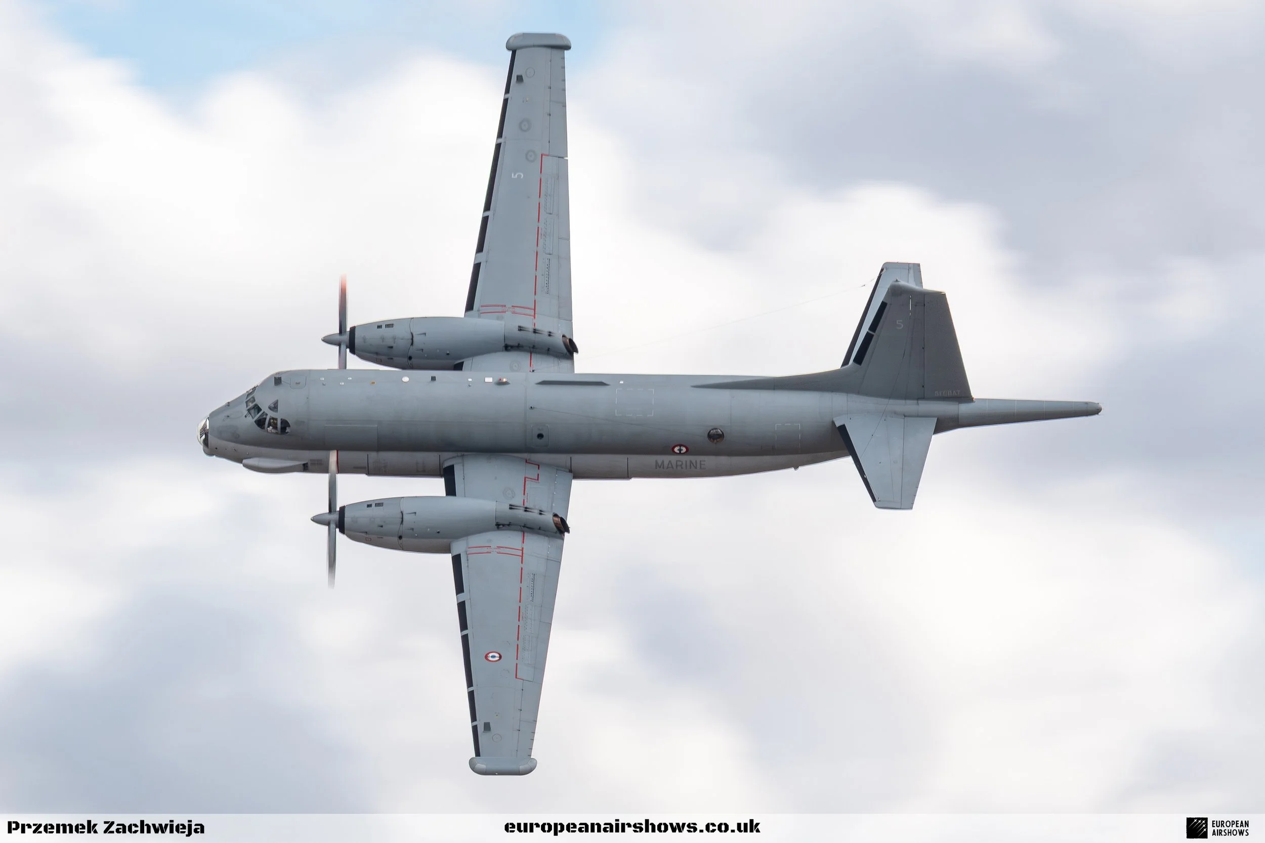 A military gray twin-engine propeller airplane flying in cloudy sky.