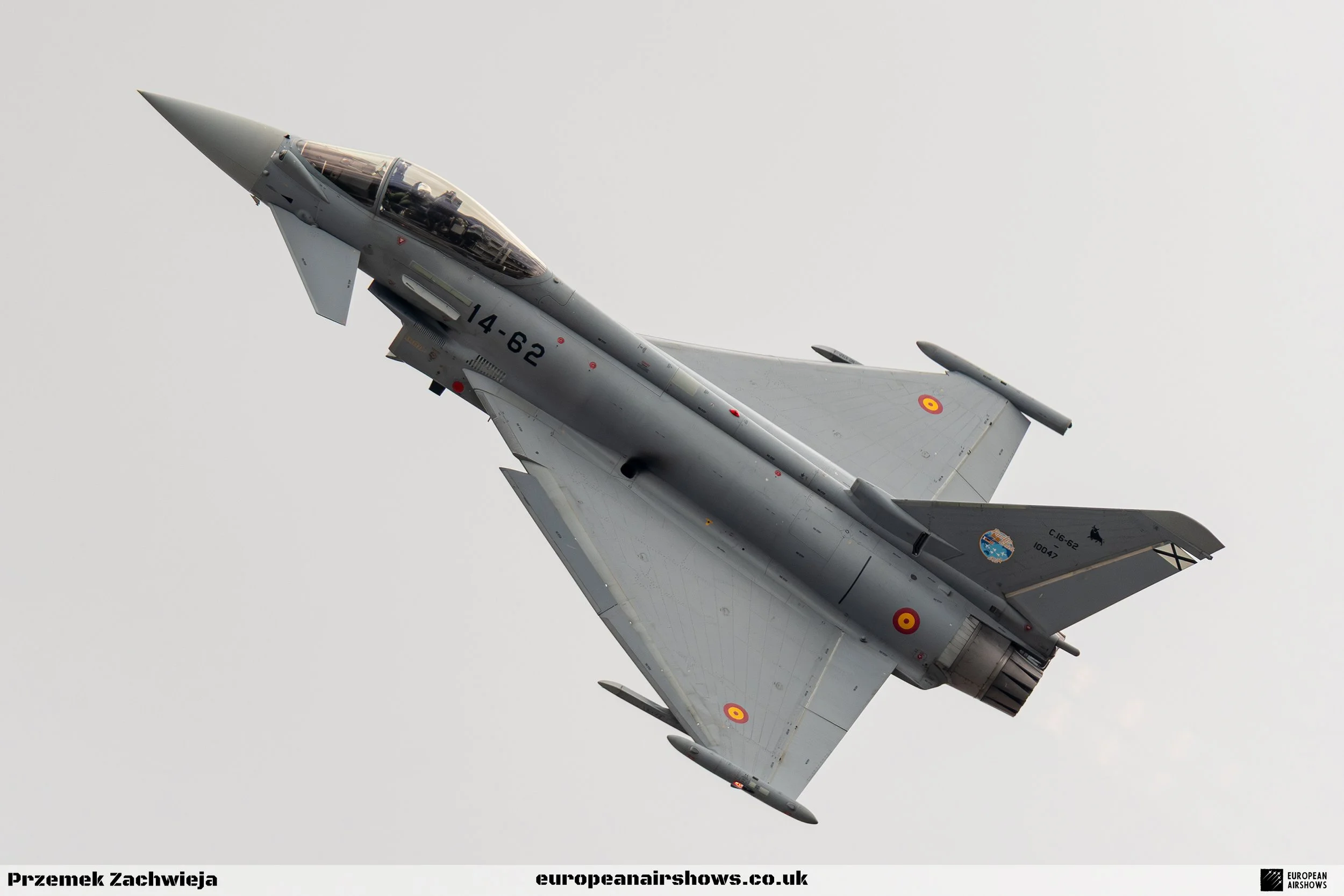 A jet fighter aircraft flying in the sky with gray camouflage, marked with identification numbers and roundels.