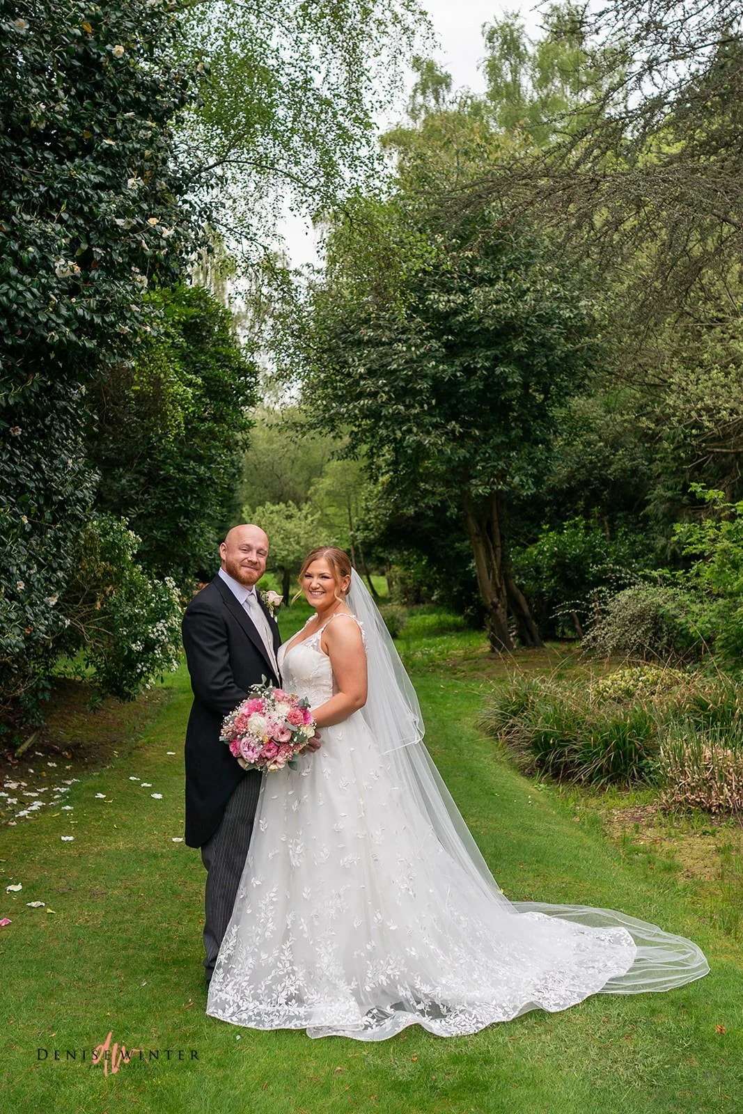 Real Boo Bride Ashley wearing her Mia Mia Babette A-line wedding dress with embroidered leaves, holding a pink and white floral bouquet, with her new husband in the grounds of Gorse Hill Hotel