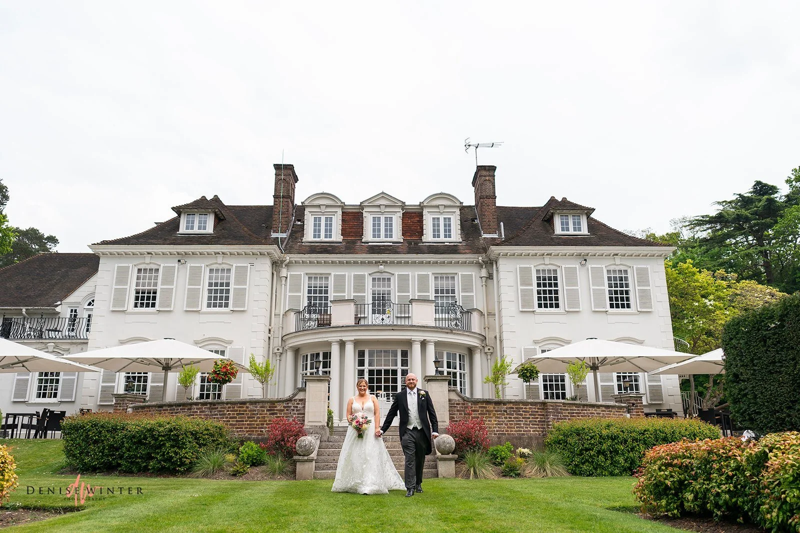 Real Boo Bride Ashley wears her Mia Mia a-line wedding dress with leaf lace detail whilst holding hands with her new husband outside Gorse Hill Hotel