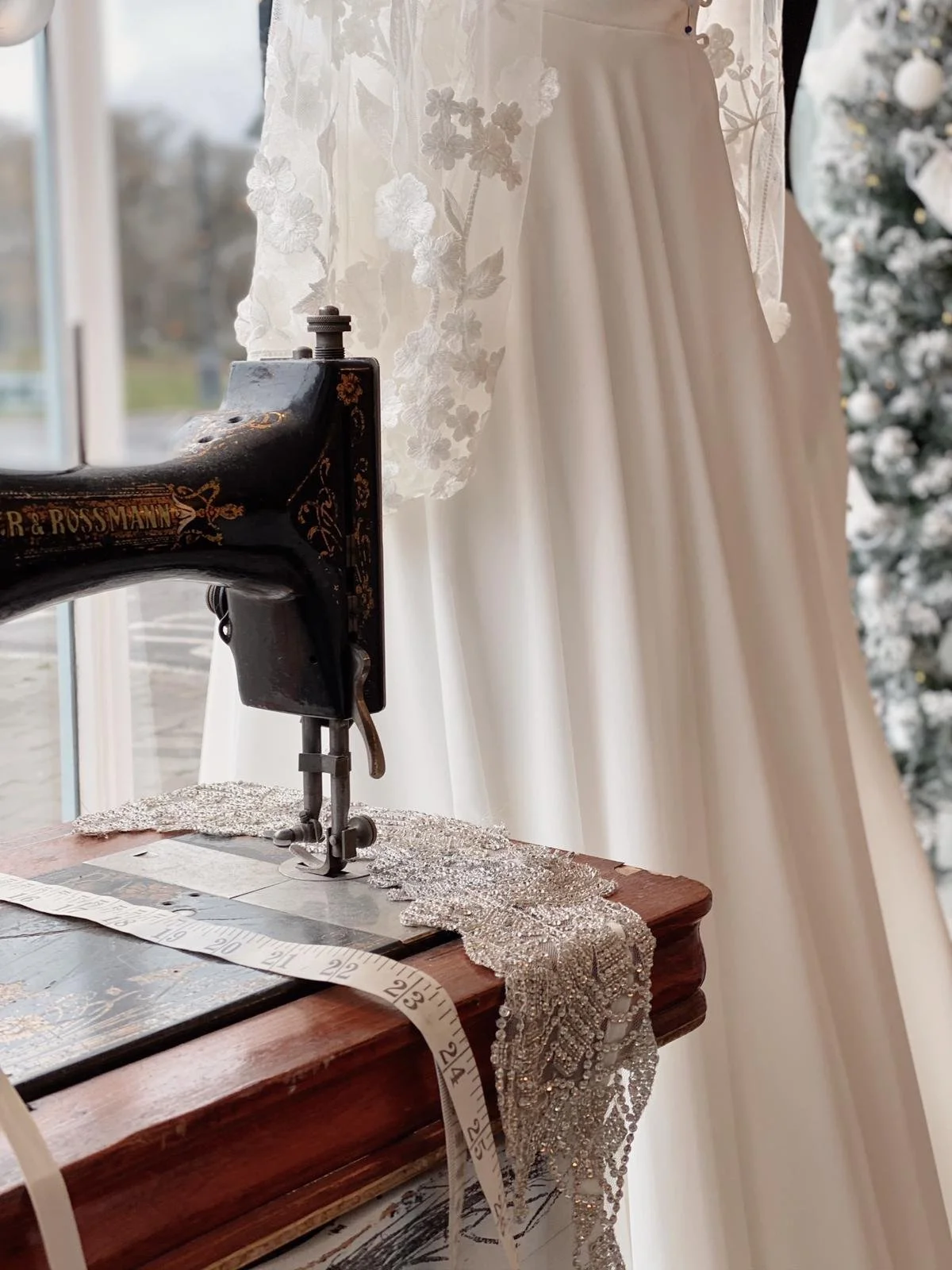 Vintage sewing machine in Boo Bridal's shop window with a tape measure and a beautiful lace wedding dress in the background