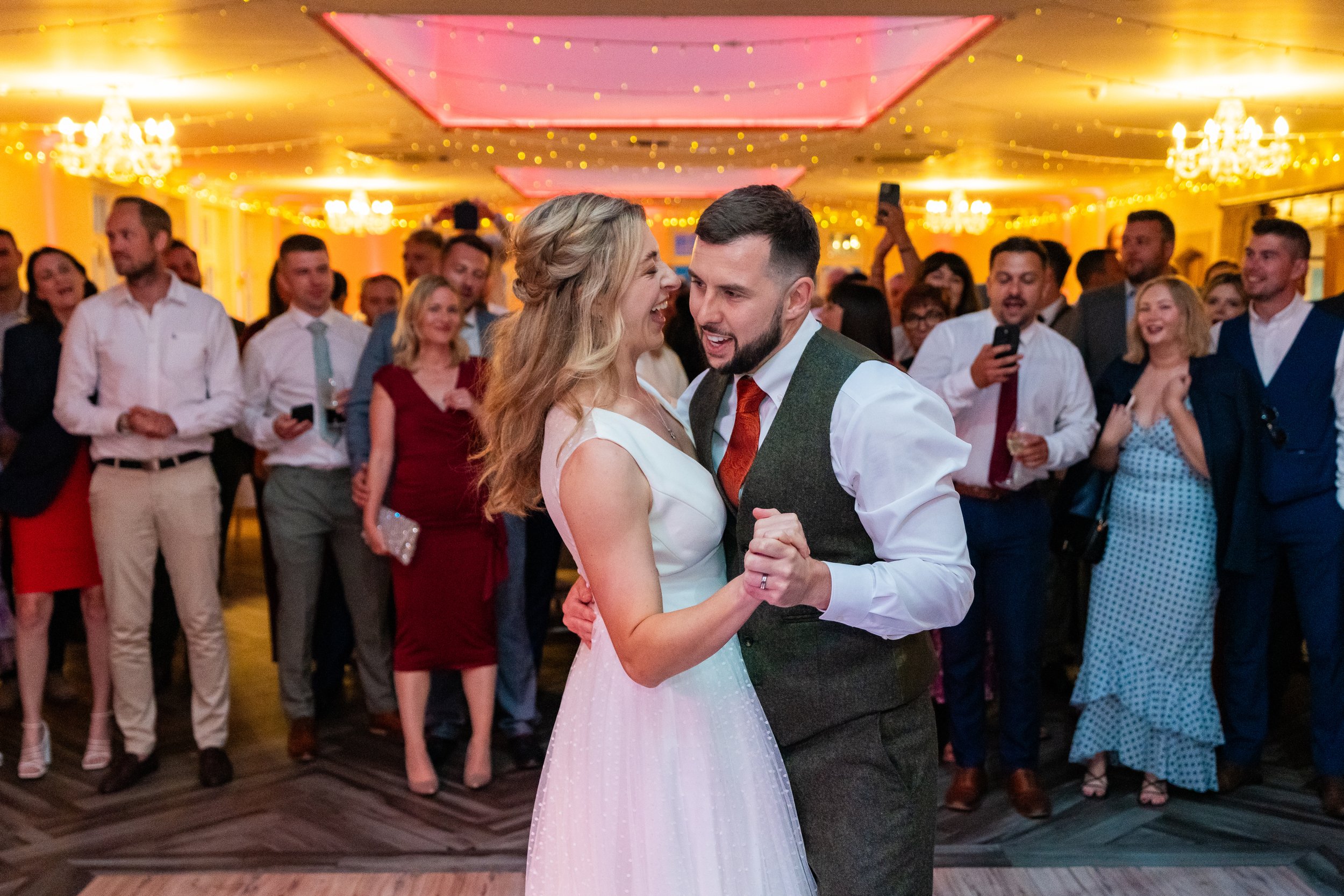 bride and groom celebrating their first dance on their wedding day surrounded by family.  Bride is wearing a sassi holford wedding dress from Boo Bridal