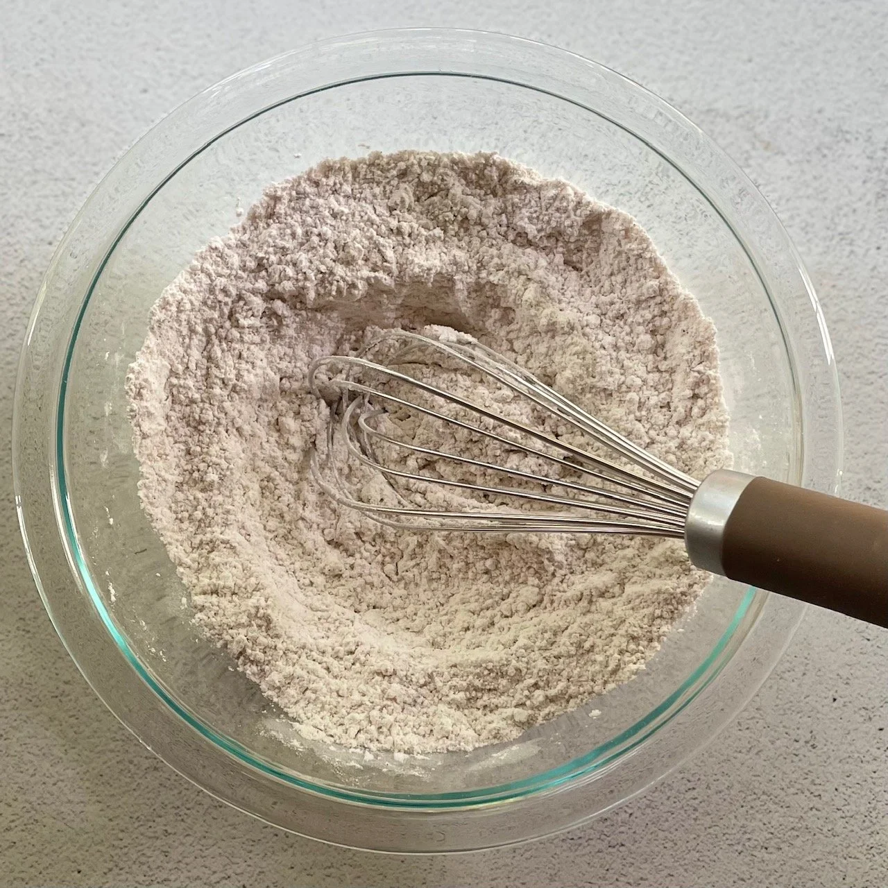 Whisking together dry ingredients in a glass bowl with a wire whisk to make pumpkin peanut butter cookies.