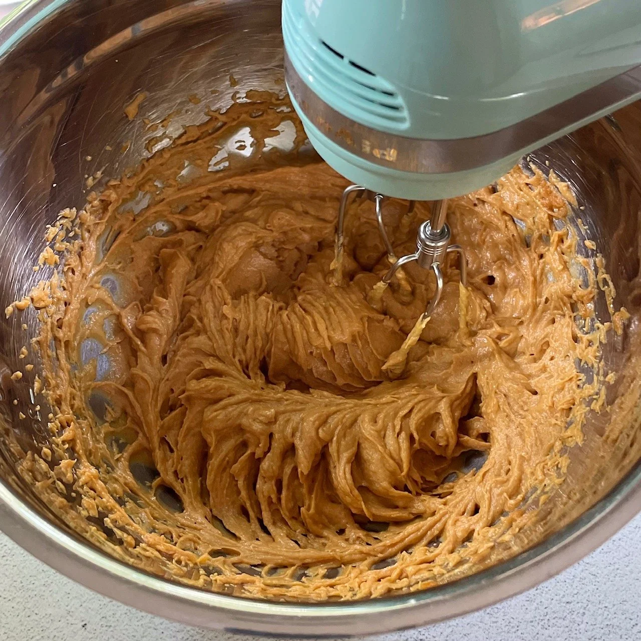 Mixing together pumpkin, peanut butter, egg, maple syrup and oil in a large stainless steel bowl with electric mixer to make pumpkin cookies for fall.