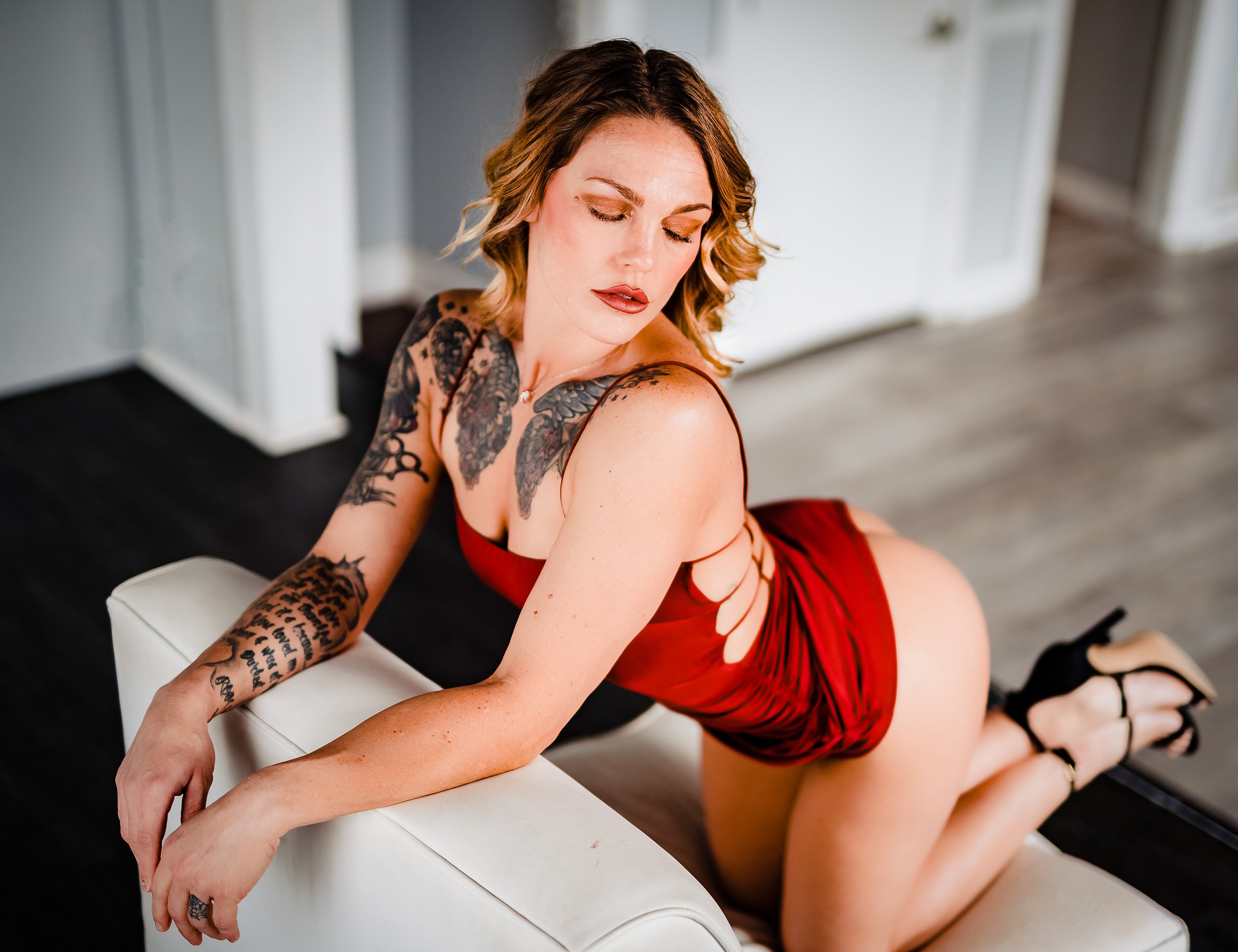 Woman in red lingerie with tattoos leaning on a white couch.