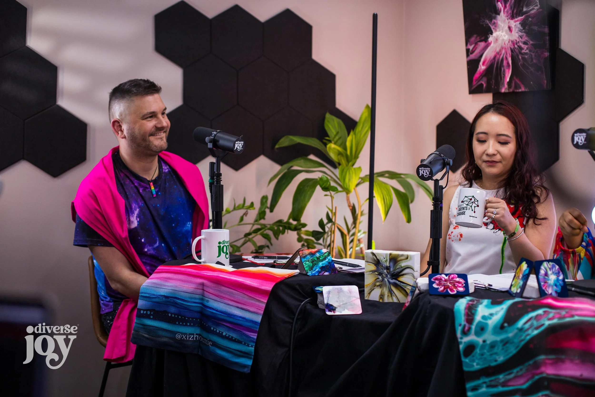 A still photo from the recording session showing Will smiling while listening to Amber offscreen and Xizhou enjoying coffee from an Inequity Agents of Change mug