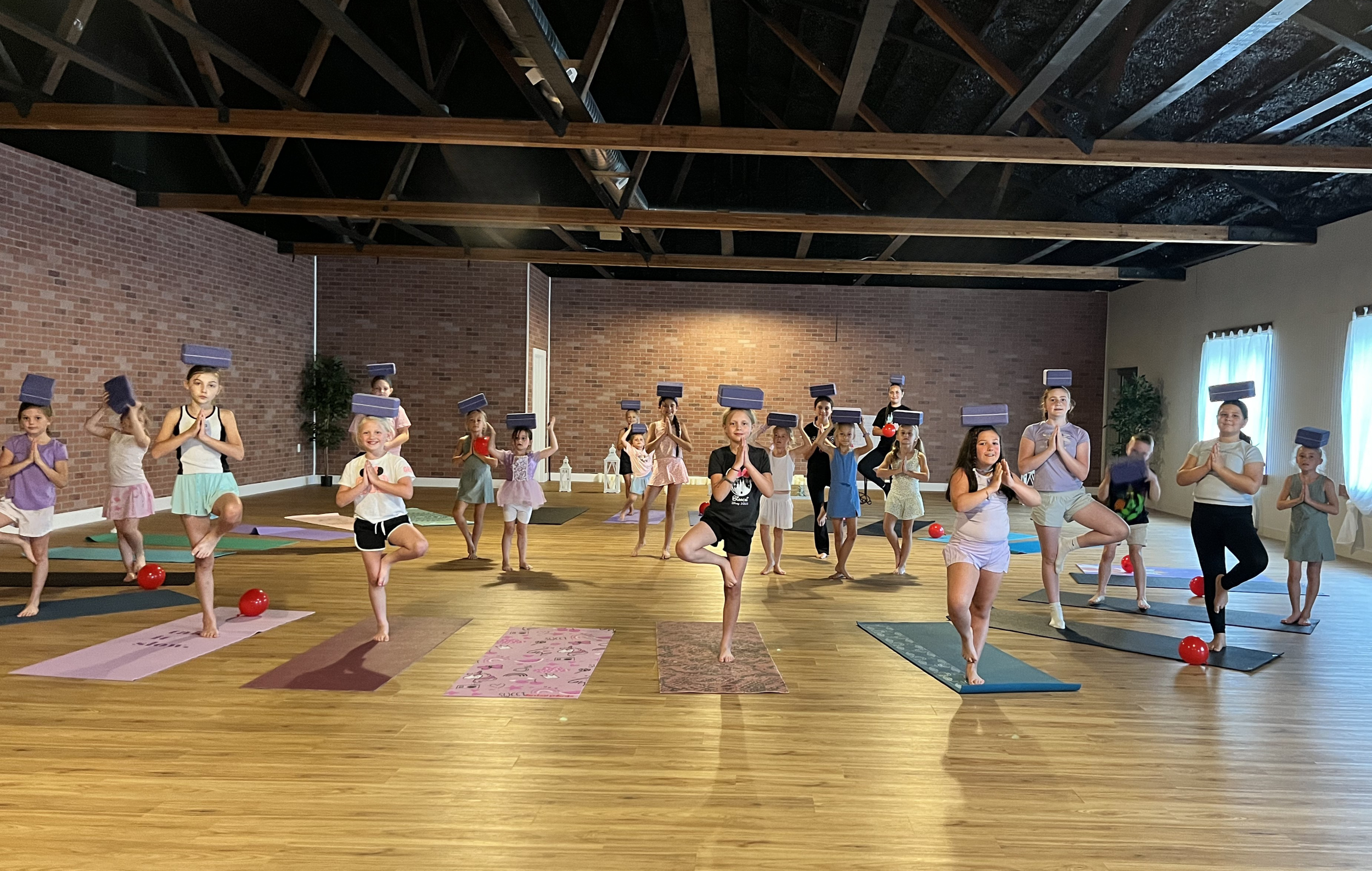 Children practicing Tree Pose with yoga blocks balanced on their heads during Disney-inspired Kids Yoga Camp at Jaya Yoga Studio in Clarks Summit, PA.