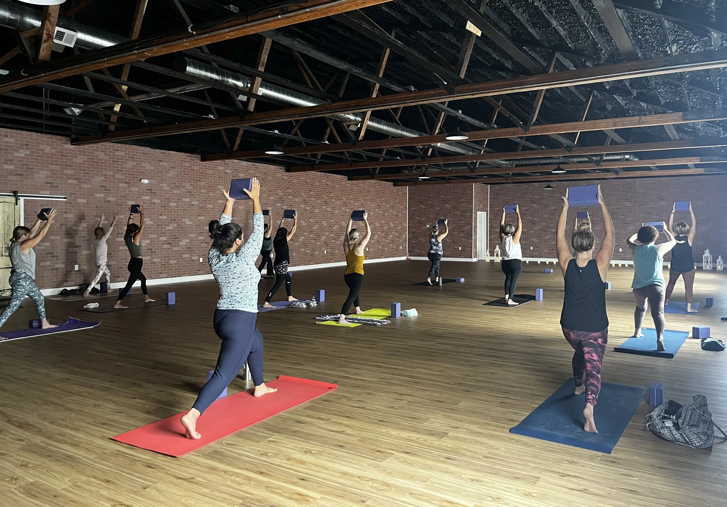 Students practicing high lunge with a block overhead at Jaya Yoga, focusing on strength, balance, and mindful movement.