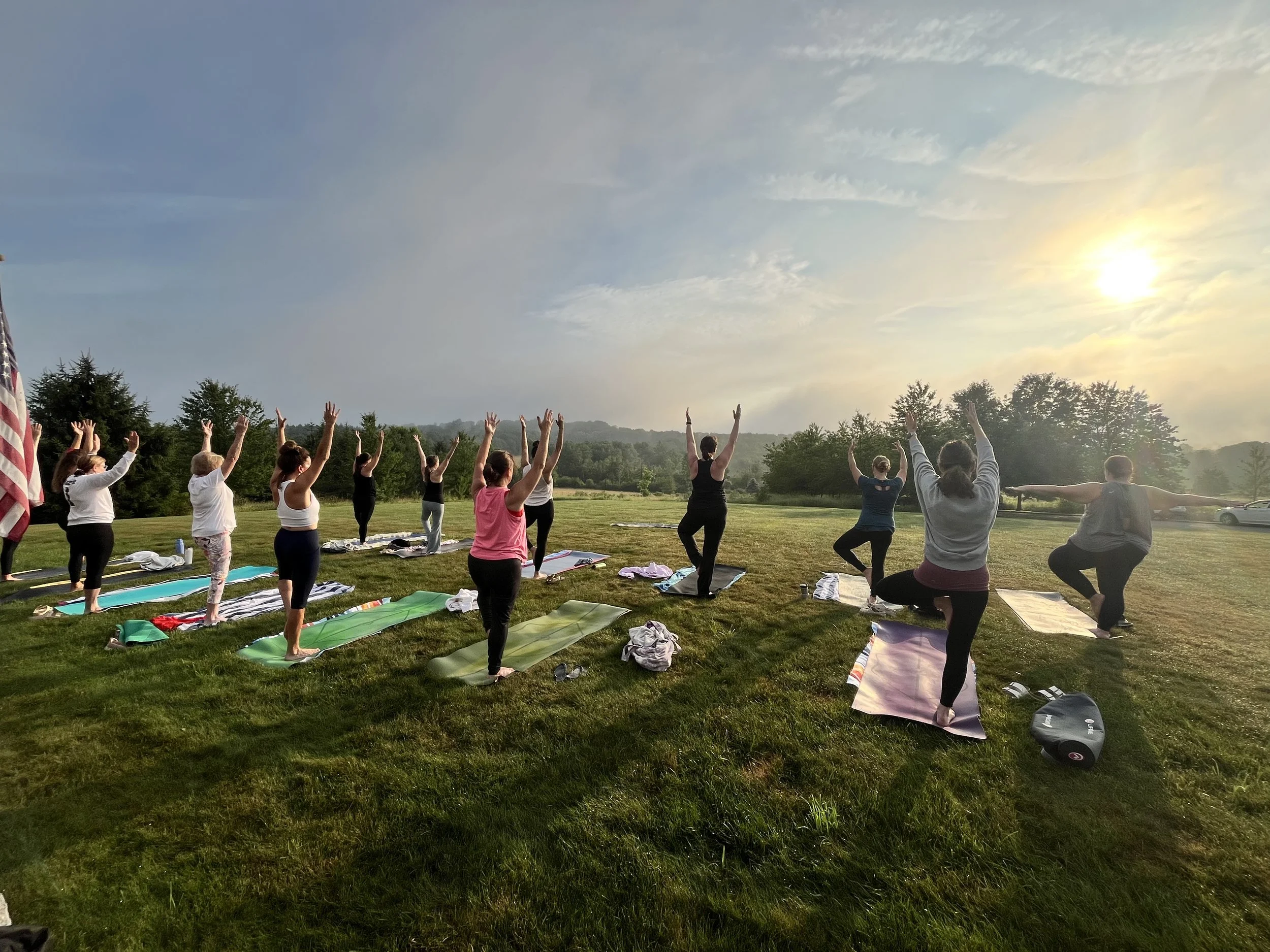 Members of the Jaya Yoga Studio community balance in Tree Pose together during an outdoor sunrise yoga practice.
