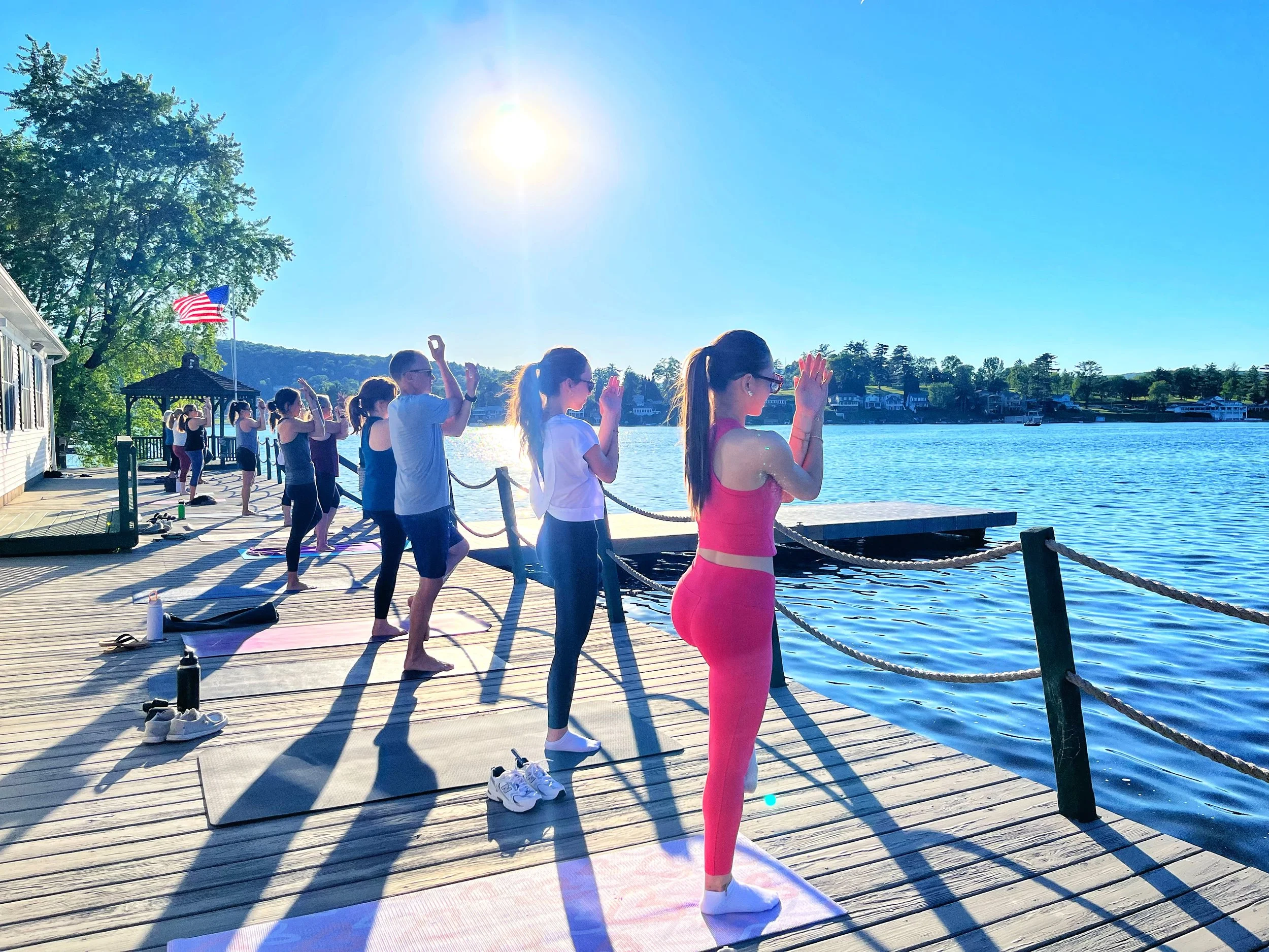 Group of students practicing Eagle in a Tree Pose on a dock at Lake Winola during a yoga class with Jaya Yoga Studio.