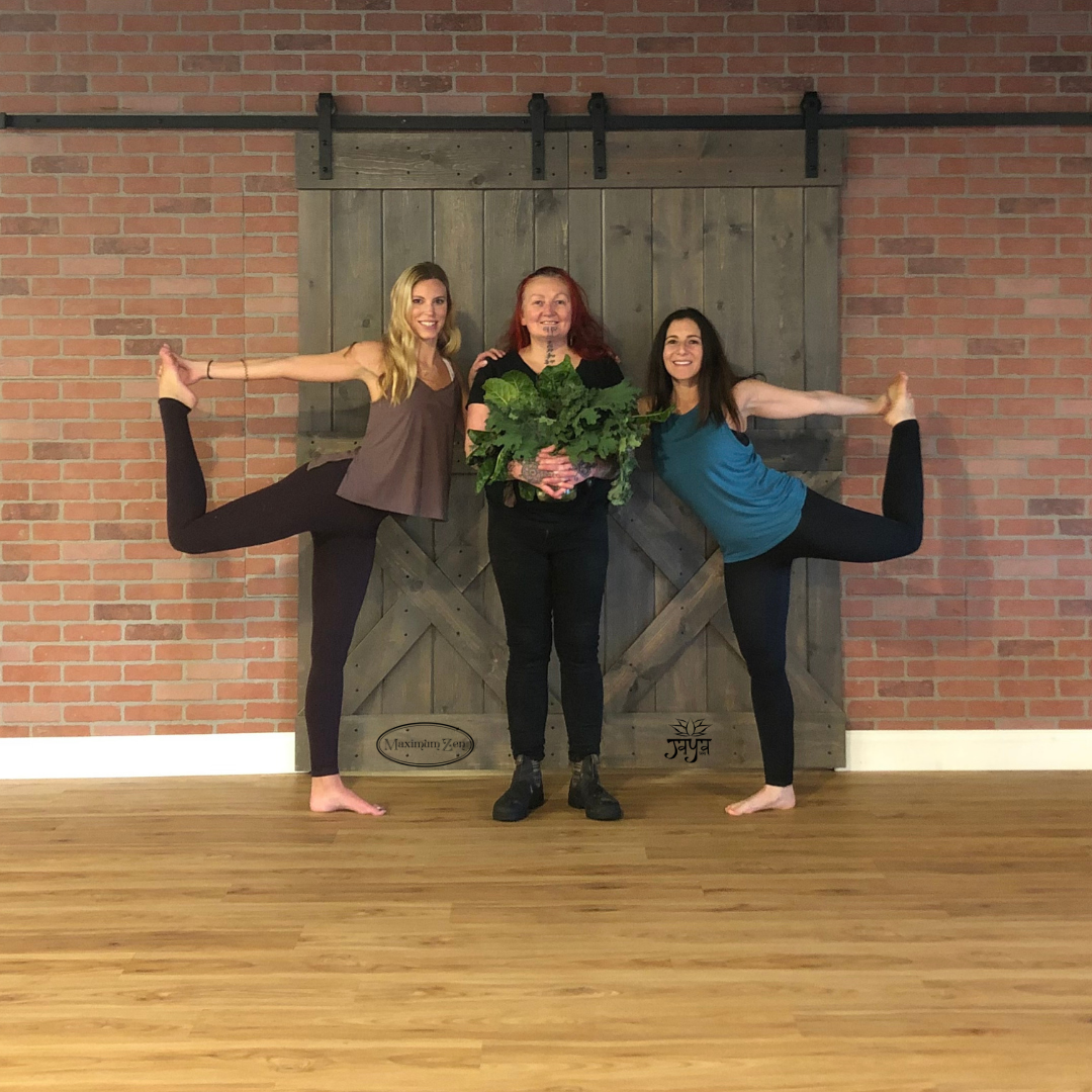 Two people demonstrating dancer pose in an outdoor setting while another person holds fresh kale, promoting a Jaya Yoga farm-to-table yoga and dinner event