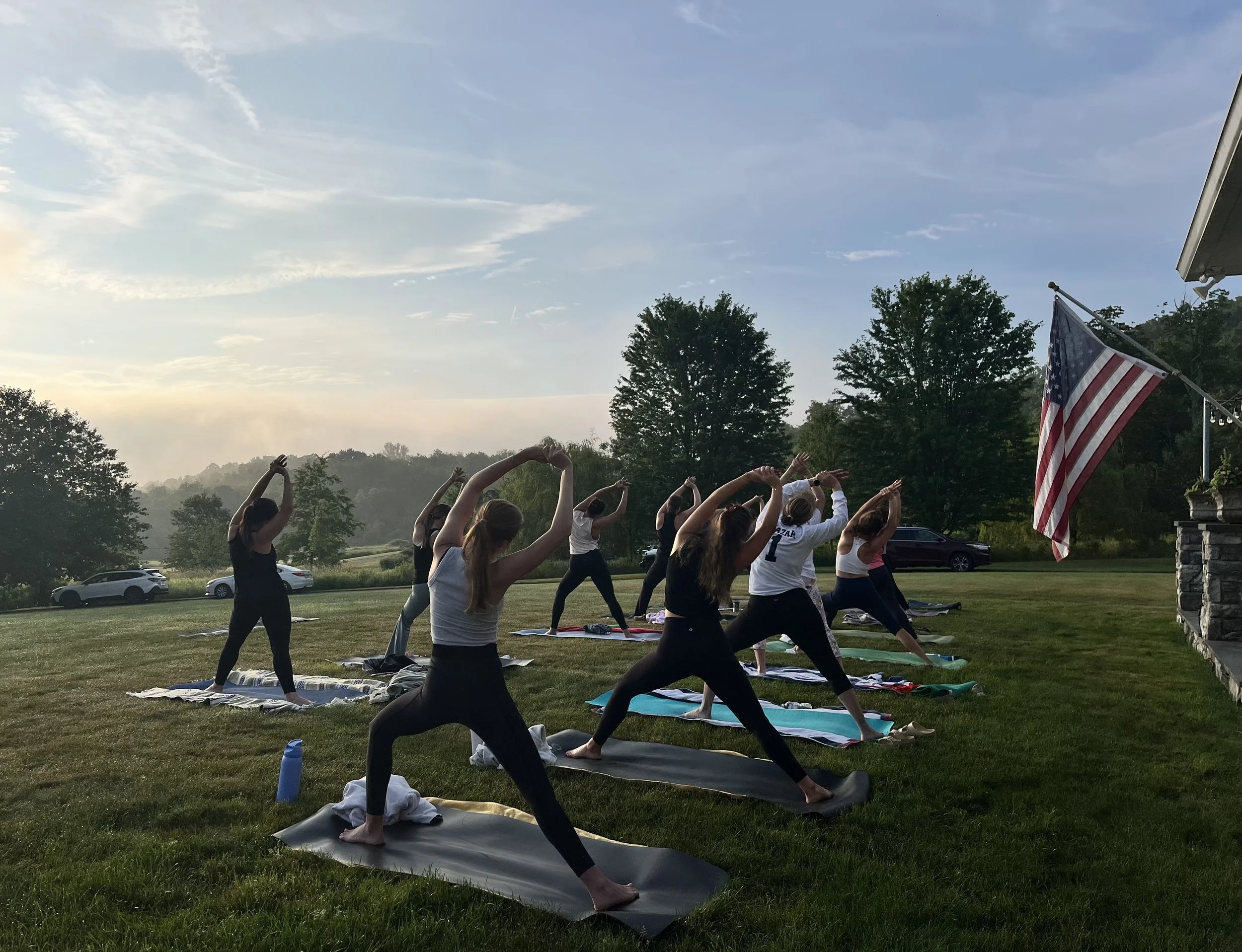 Jaya Yoga Studio students practice Warrior Pose during a peaceful sunrise yoga class on a member's lawn.
