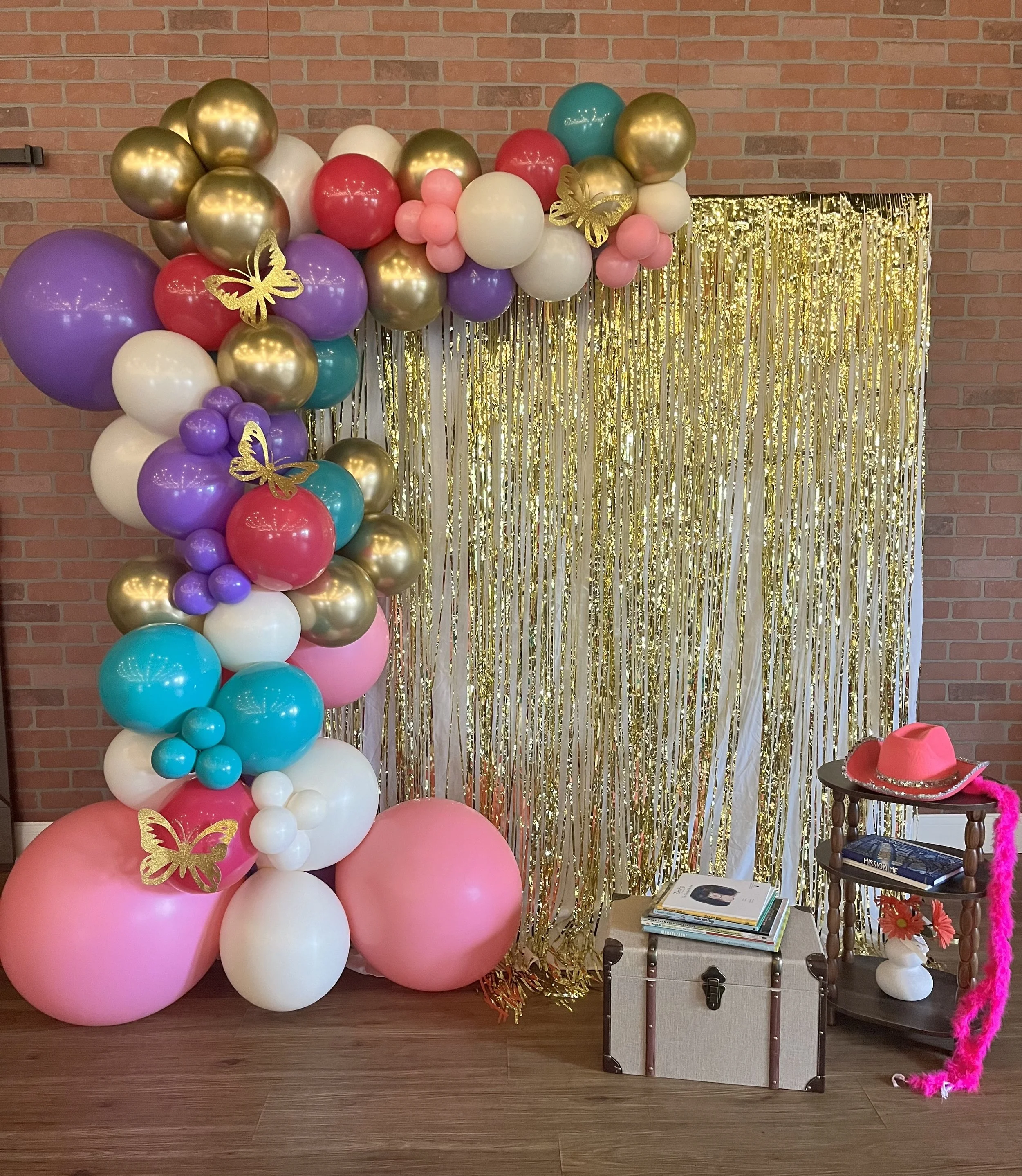 Dolly Parton Day photo booth at Jaya Yoga Studio in Clarks Summit, with a colorful balloon arch, gold fringe backdrop, butterfly decorations, and a pink cowboy hat.
