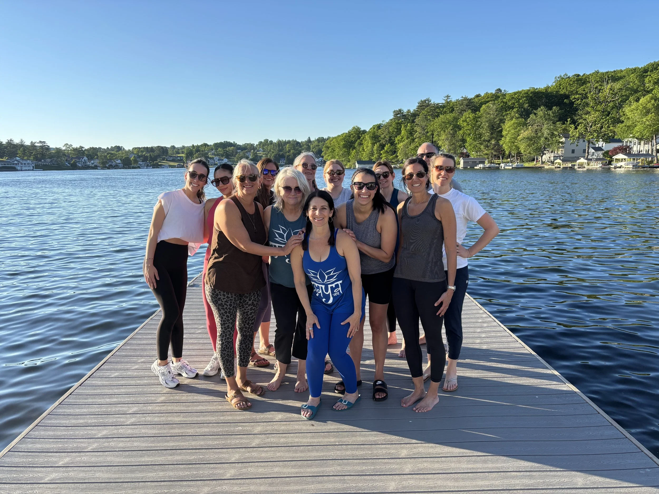 Group of people standing on a dock with trees and houses in the background after a yoga class on the dock at Lake Winola hosted by Jaya Yoga Studio.