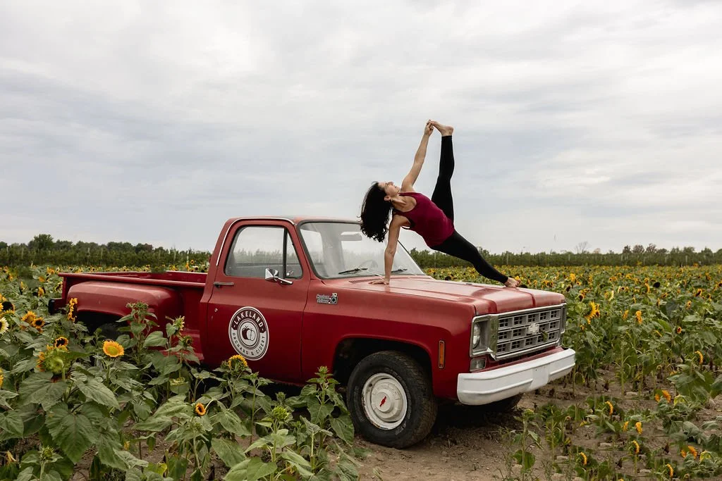 Hilary from Jaya Yoga Studio in side plank with hand holding foot outdoors balancing on the hood of a truck.