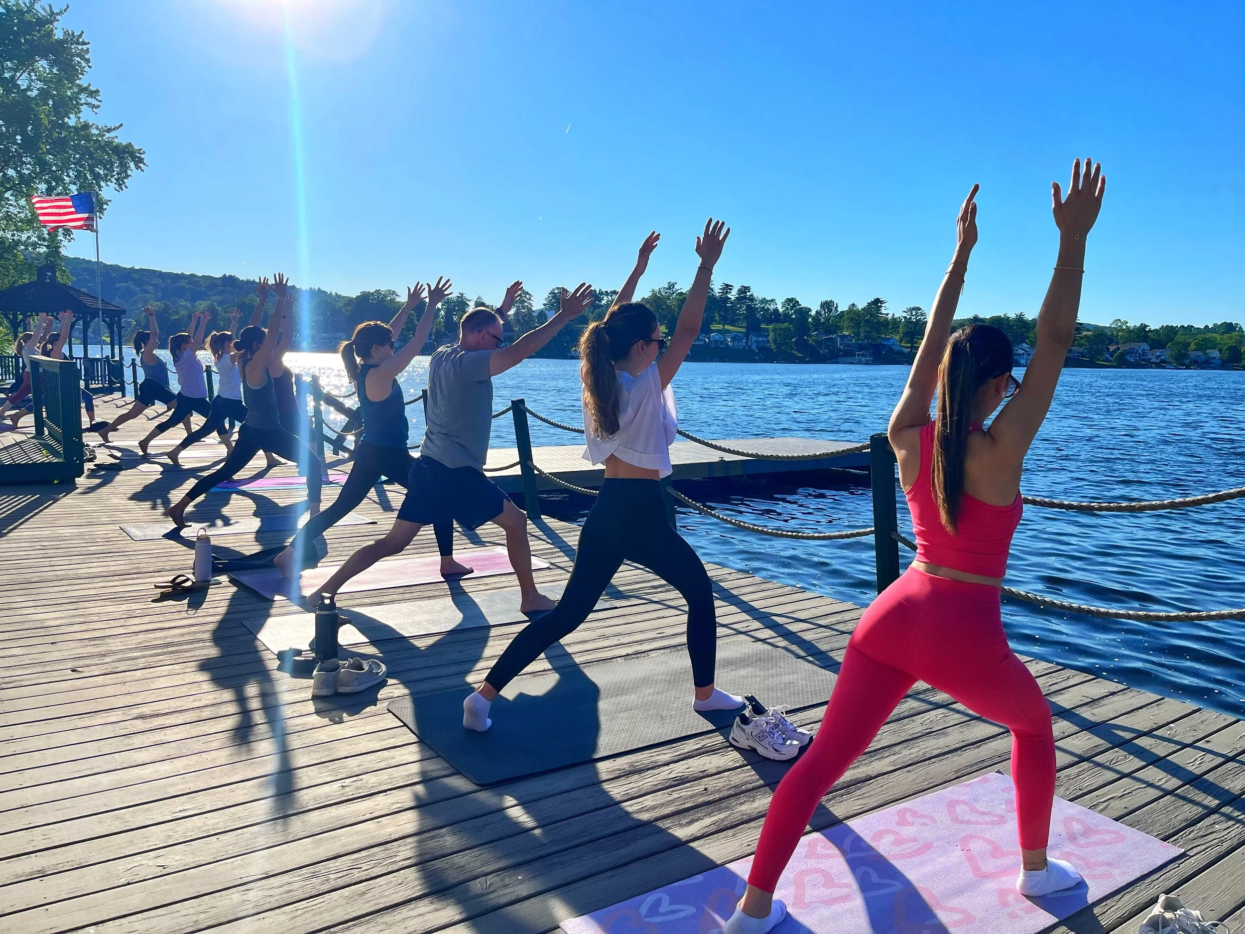 Group of students practicing High Lunge on a dock at Lake Winola during a yoga class with Jaya Yoga Studio.