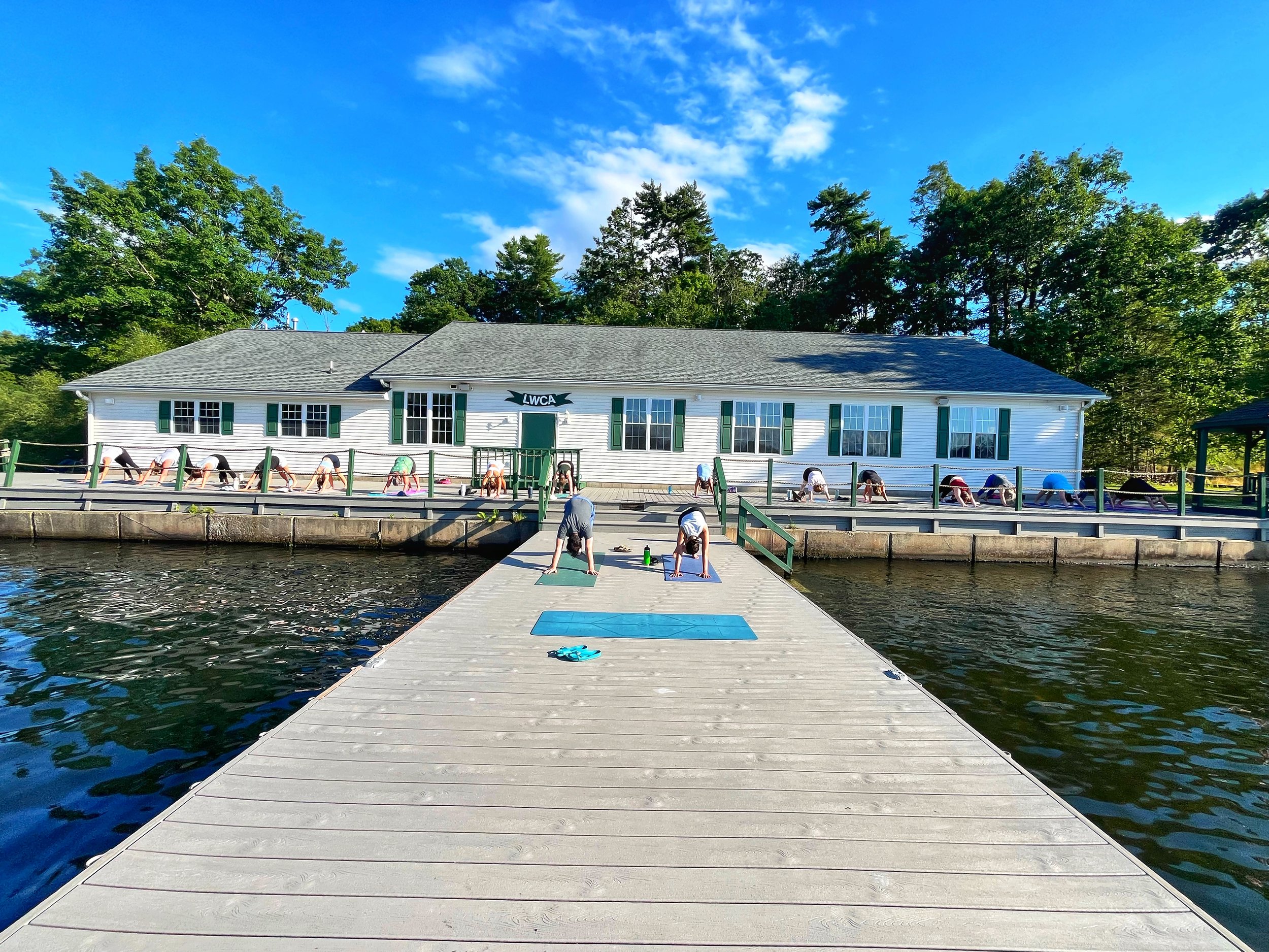 Gropu of people doing down dog on a dock at Lake Winola, led by Hilary of Jaya Yoga Studio.