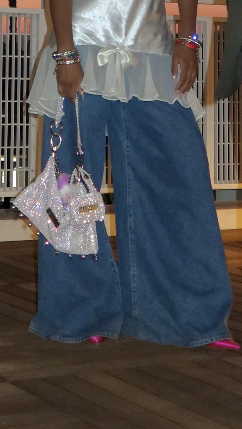 Close-up of the Baguette Bag held low beside wide-leg denim, emphasizing the bag’s slouch, crystal texture, and layered construction.